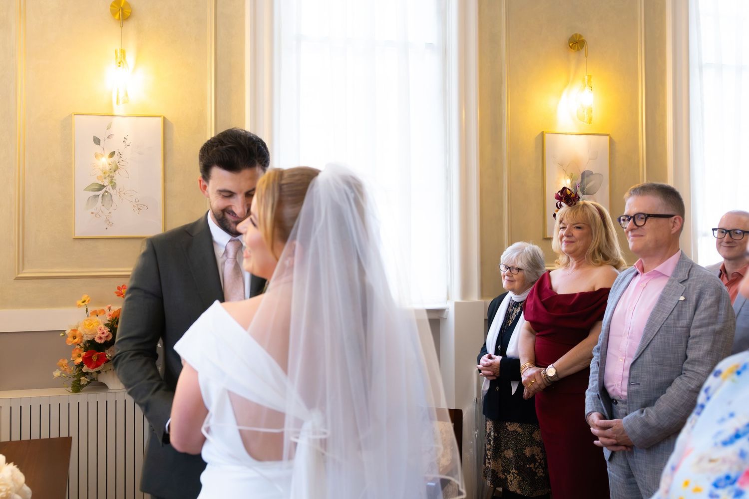 Bride and groom share an intimate moment during wedding ceremony with smiling guests watching in elegant venue.