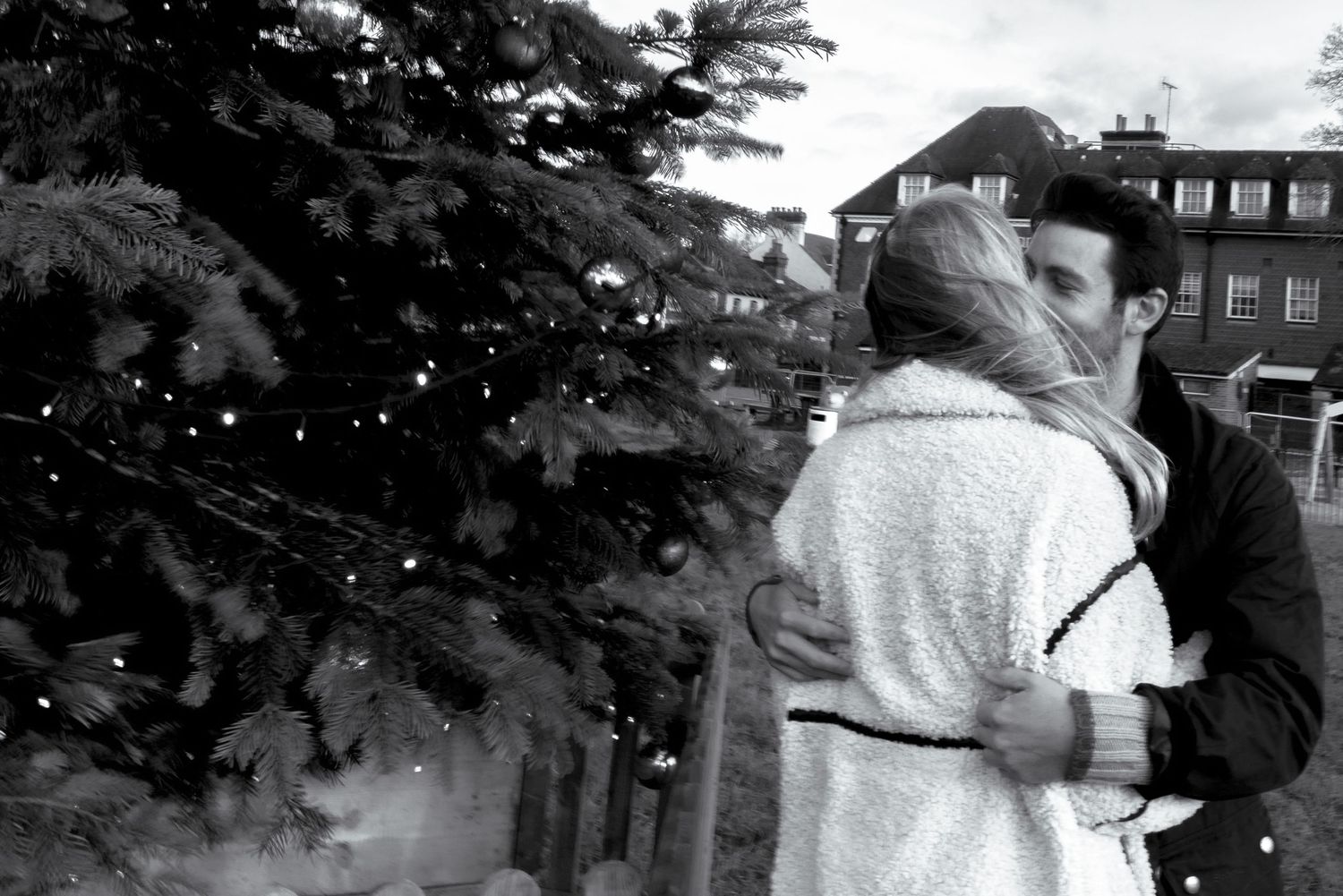 A couple in winter attire shares a tender moment outdoors against a dark background.