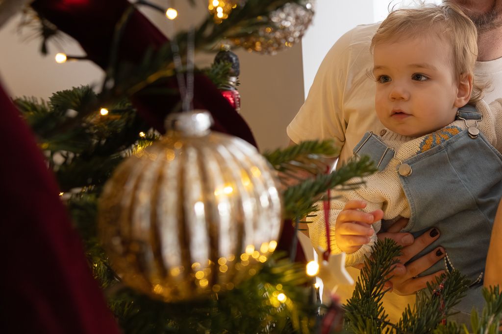 A close-up of a large gold Christmas ornament with a child and tree in soft focus background.