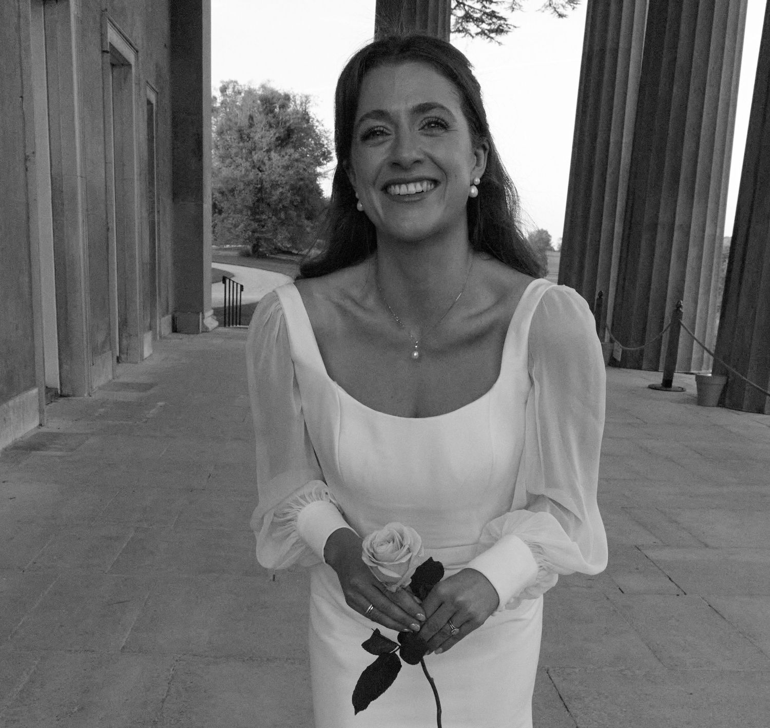 Candid moments of a bride with a rose captured in black and white on a columned porch.