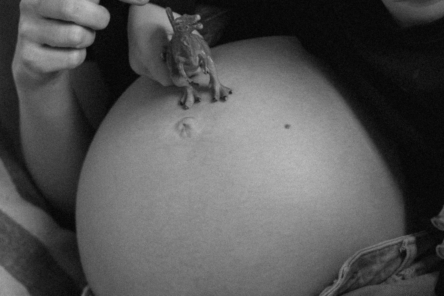 Black and white photo of a pregnant belly with a small dinosaur toy placed on top.