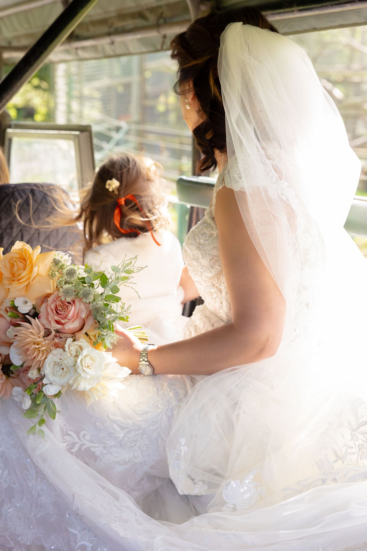 Close-up details of a bride's white lace wedding dress with a delicate bouquet of pink and peach roses.
