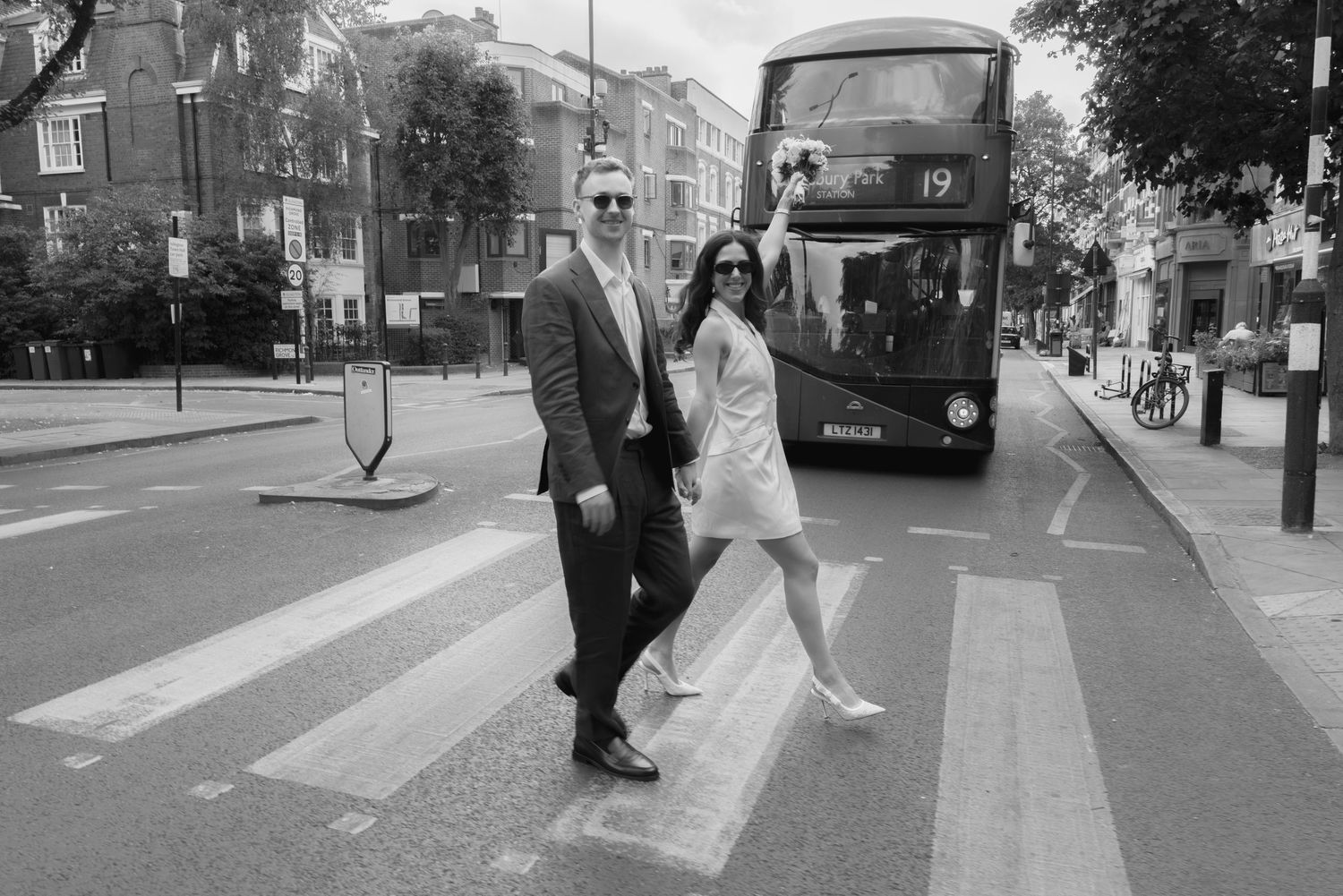 Couple posing on a zebra crossing in London with a double-decker bus behind them in black and white.