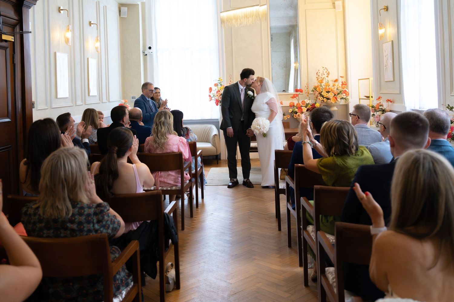 Bride and groom stand at the altar during an elegant indoor wedding ceremony with guests seated in wooden pews.