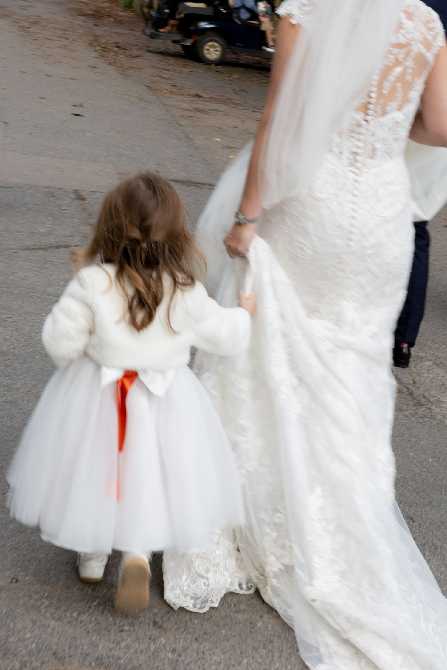 Young flower girl in white dress following a flowing wedding gown train.