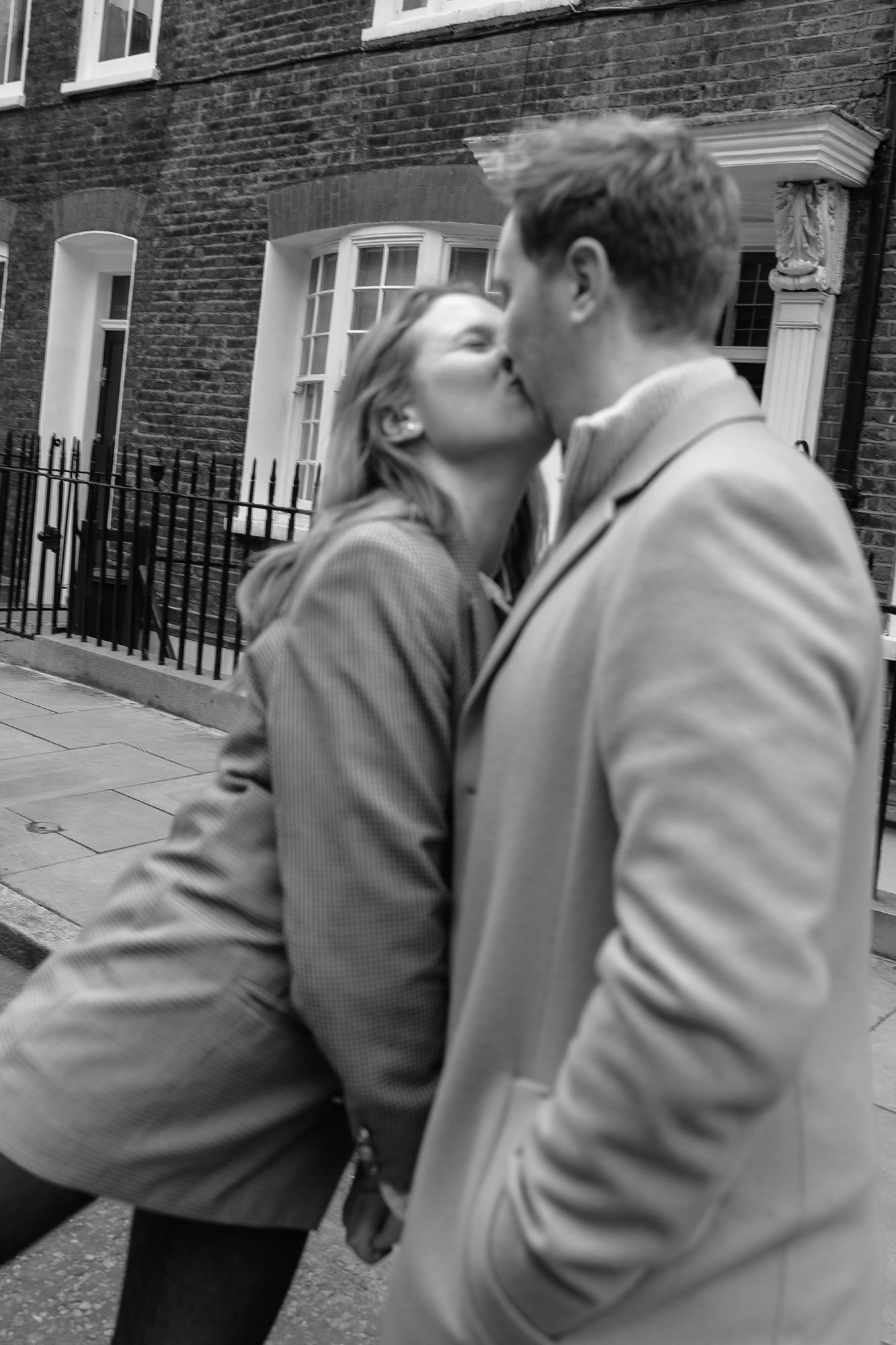 Black and white photo of a couple sharing an intimate moment against brick architecture.