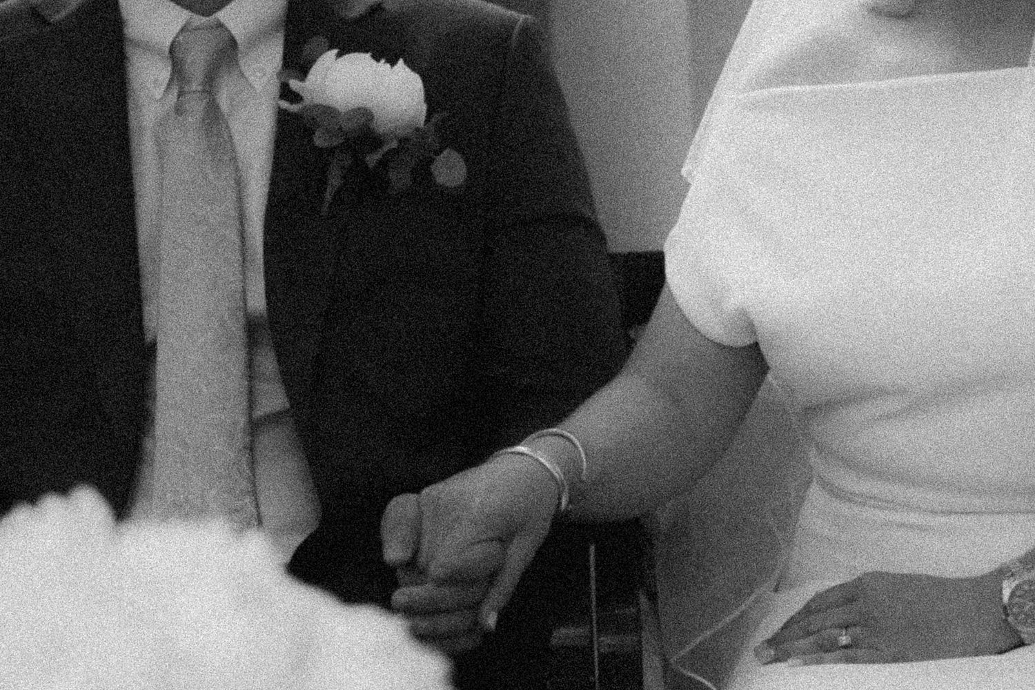 Black and white wedding photo of bride and groom holding hands during ceremony.