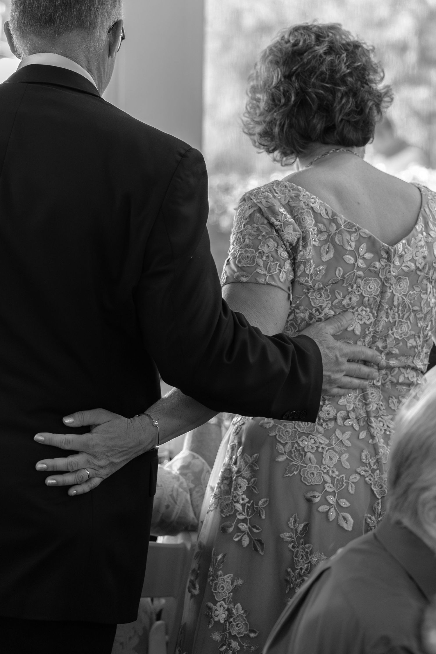 Black and white photo of a couple walking arm in arm at a wedding ceremony.