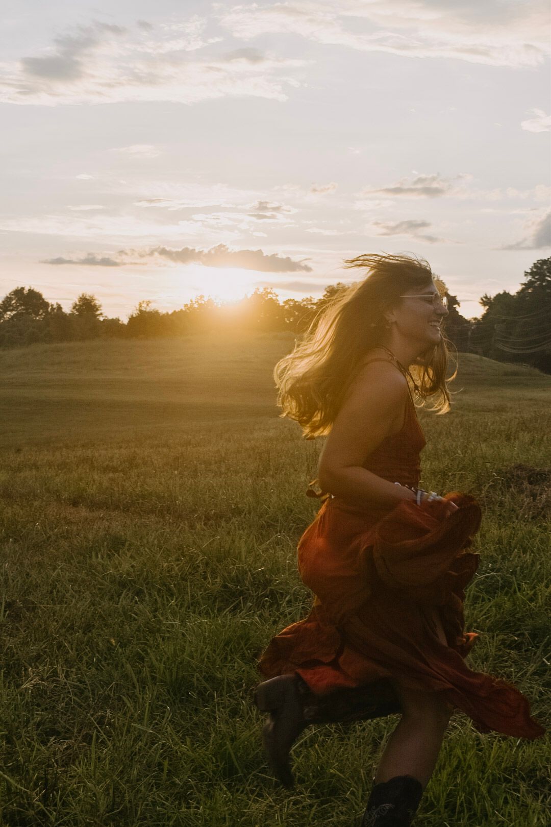 A silhouette dances in a flowing dress across a golden field at sunset as wind sweeps through their hair.