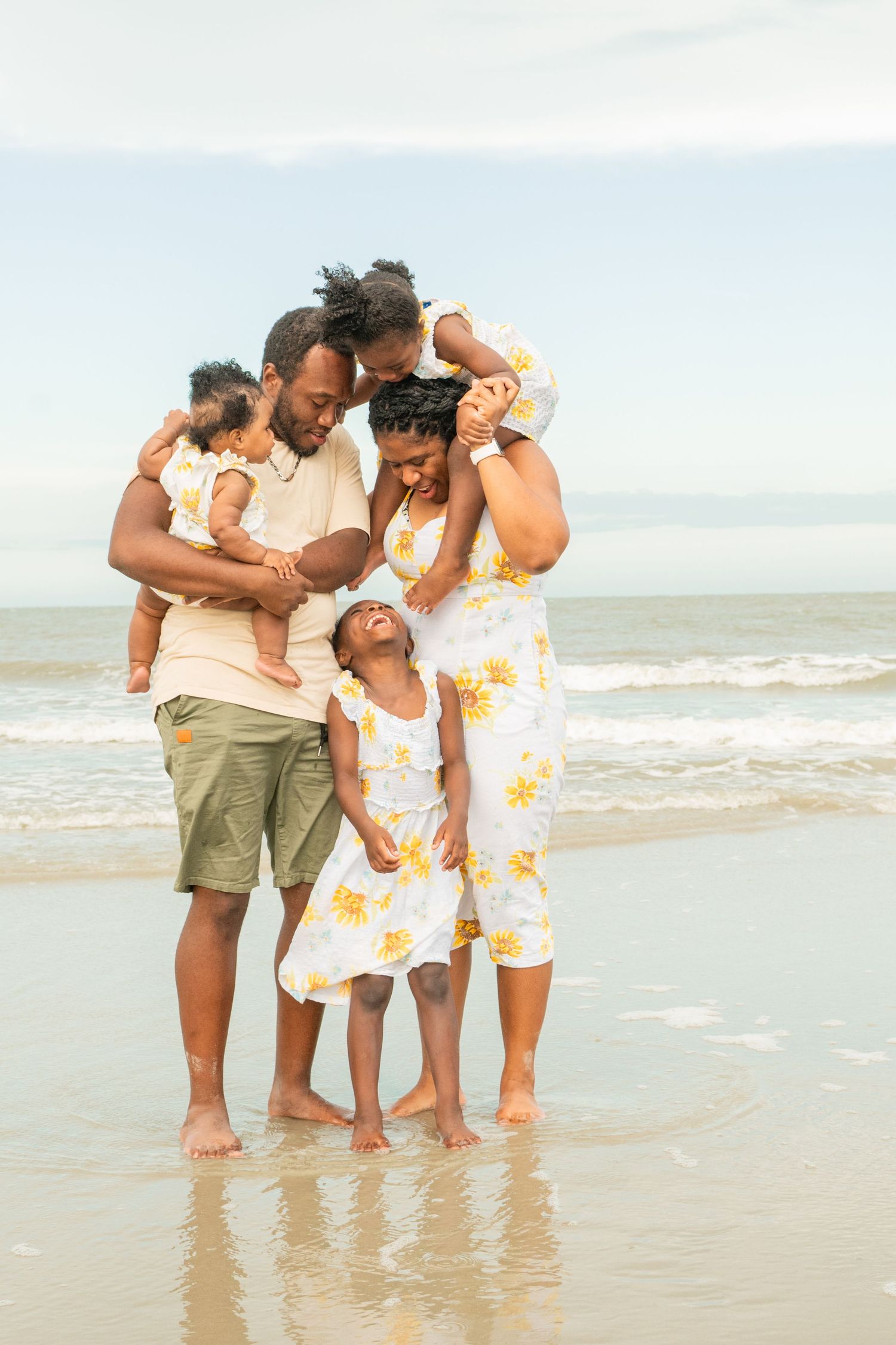 A loving family shares a joyful moment together on the beach at sunset with waves and sand in the background.
