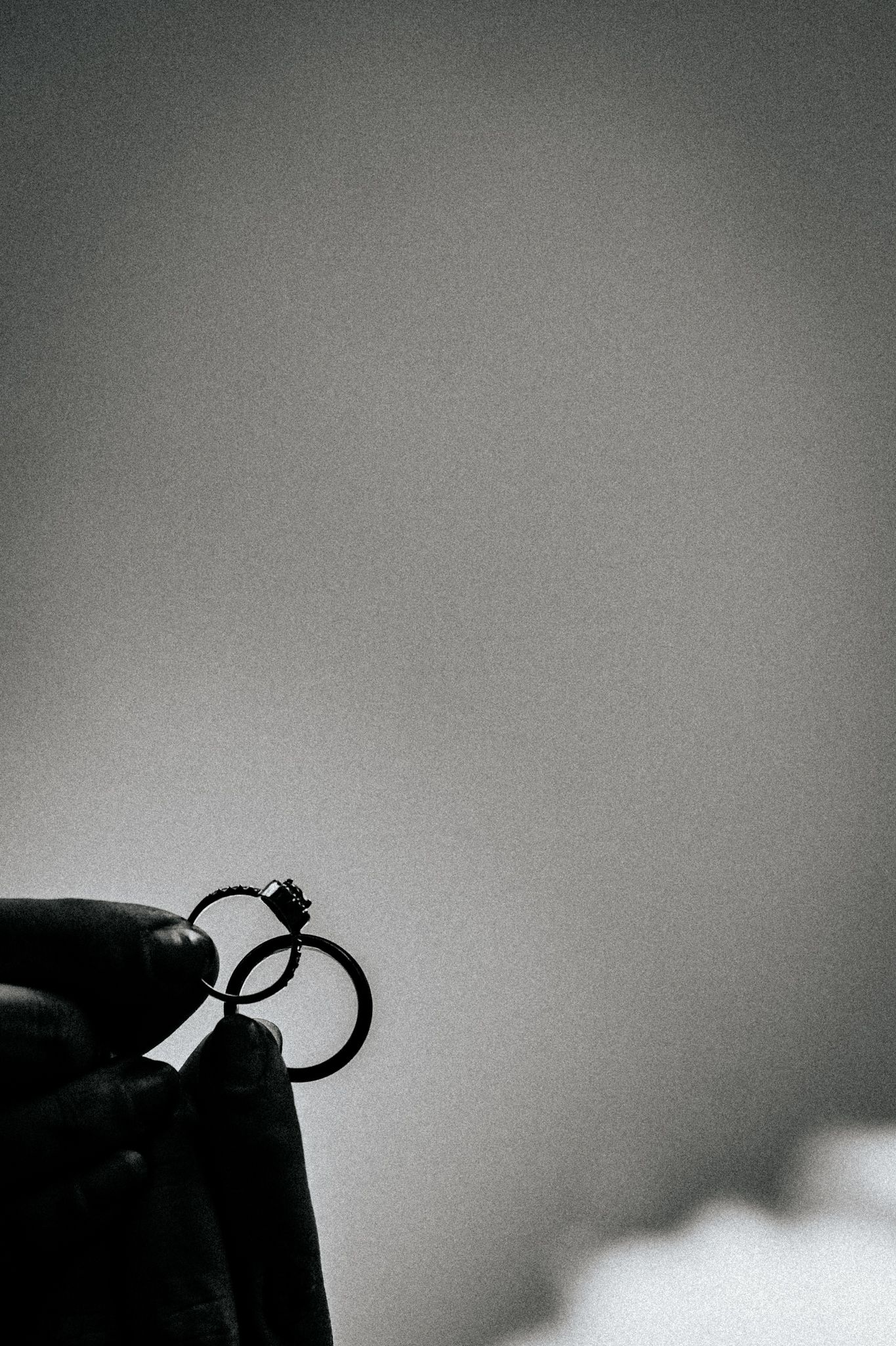 Black and white silhouette of a ring being held against a grey gradient background.