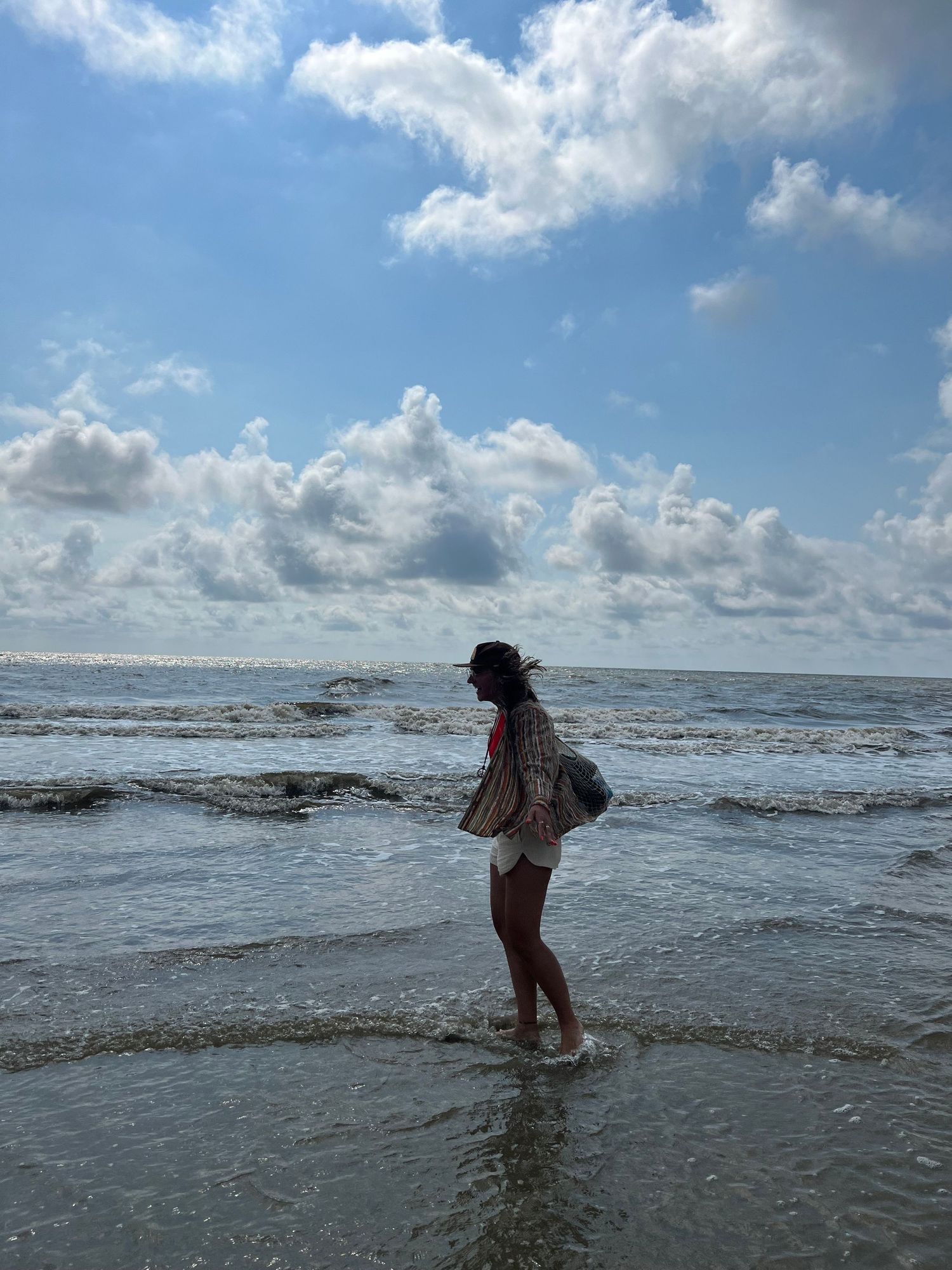 A person explores shallow ocean waves at the beach under a bright cloudy sky in this four-image sequence.