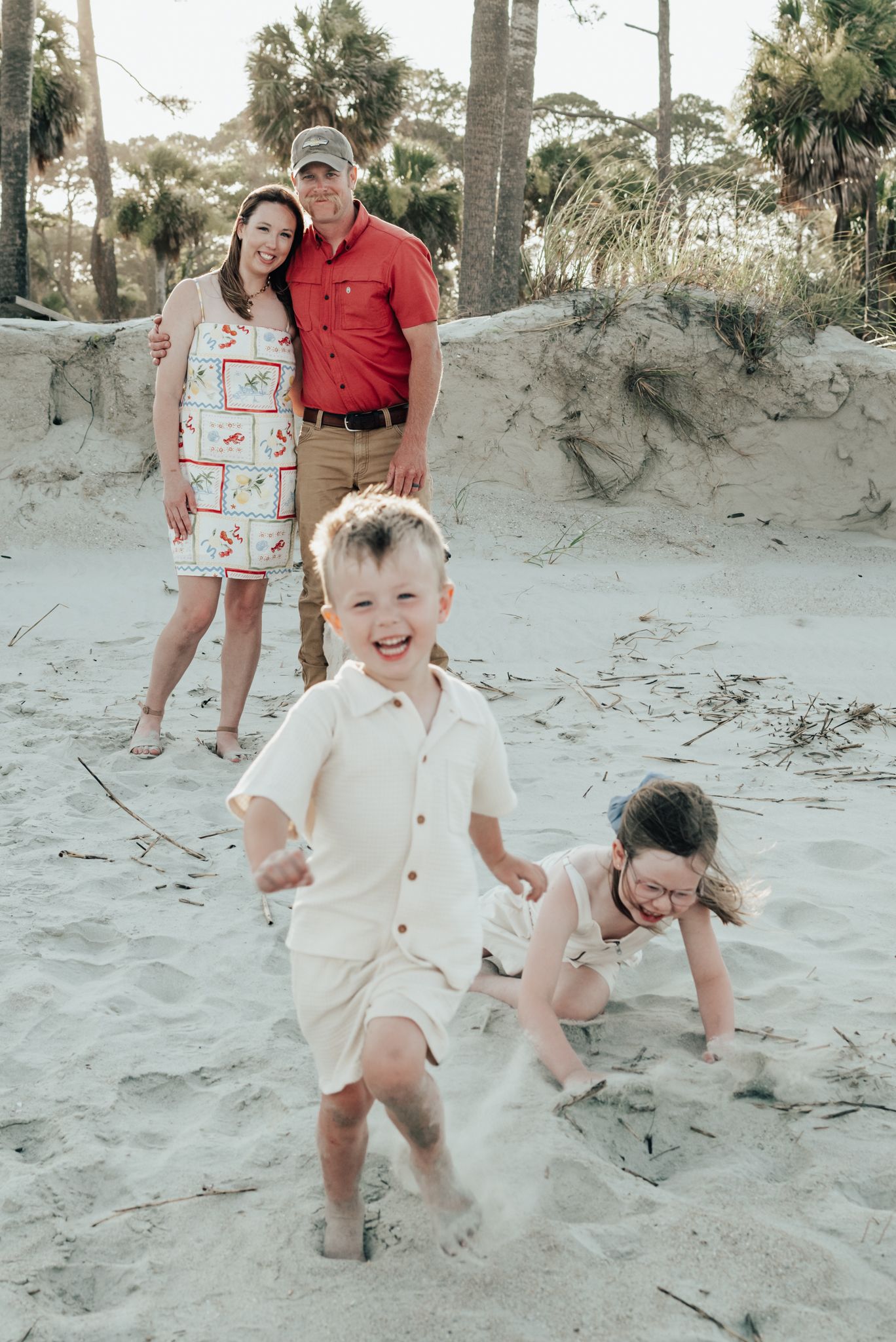 Casual family photoshoot at a sandy beach showing playful moments as kids jump and create movement in the sand.