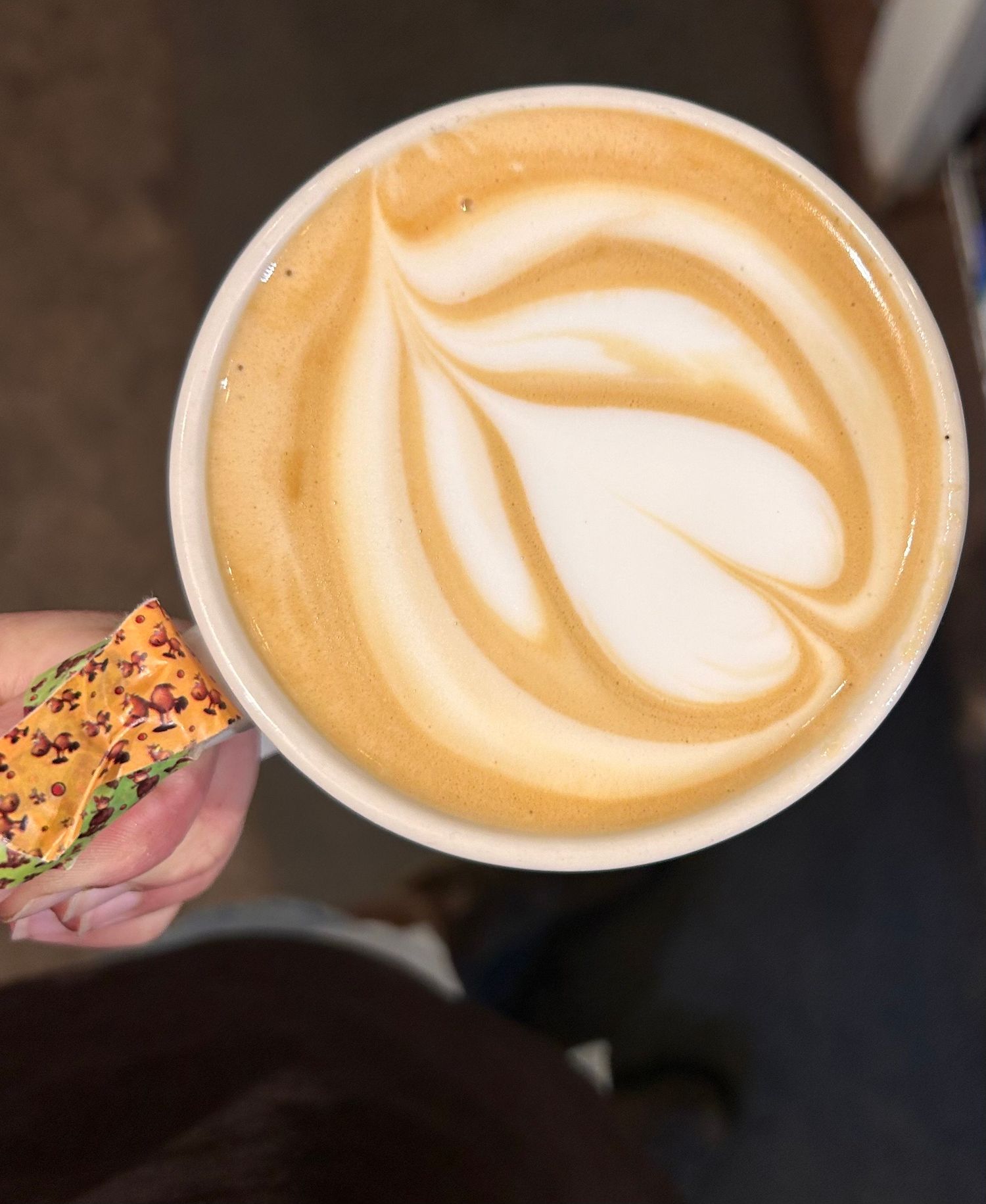 A white ceramic cup of latte with intricate heart-shaped latte art and a decorated pastry or snack bar on the side.