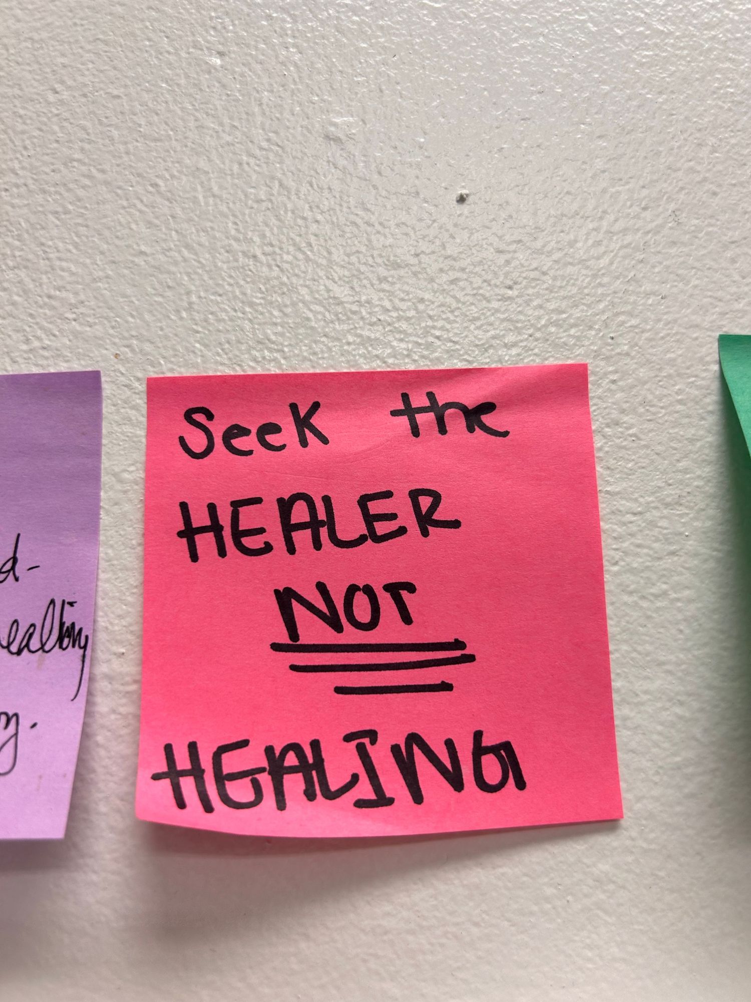 Close-up of pink sticky notes on a wall with one labeled 'HEALER' and 'NOT FIGHTING' written in black marker.