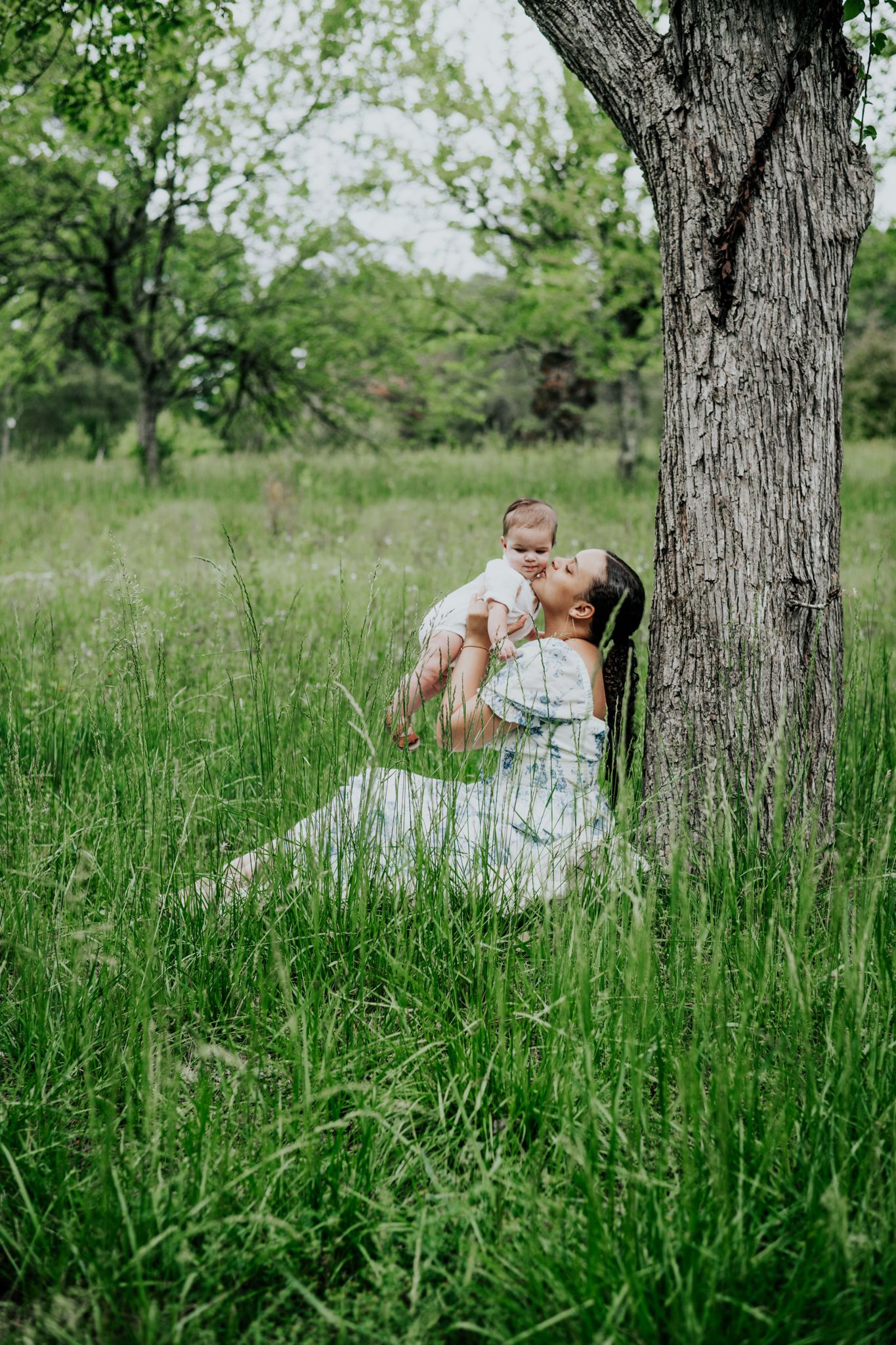 A tender moment captured in a lush green field beneath a large tree on a bright spring day.