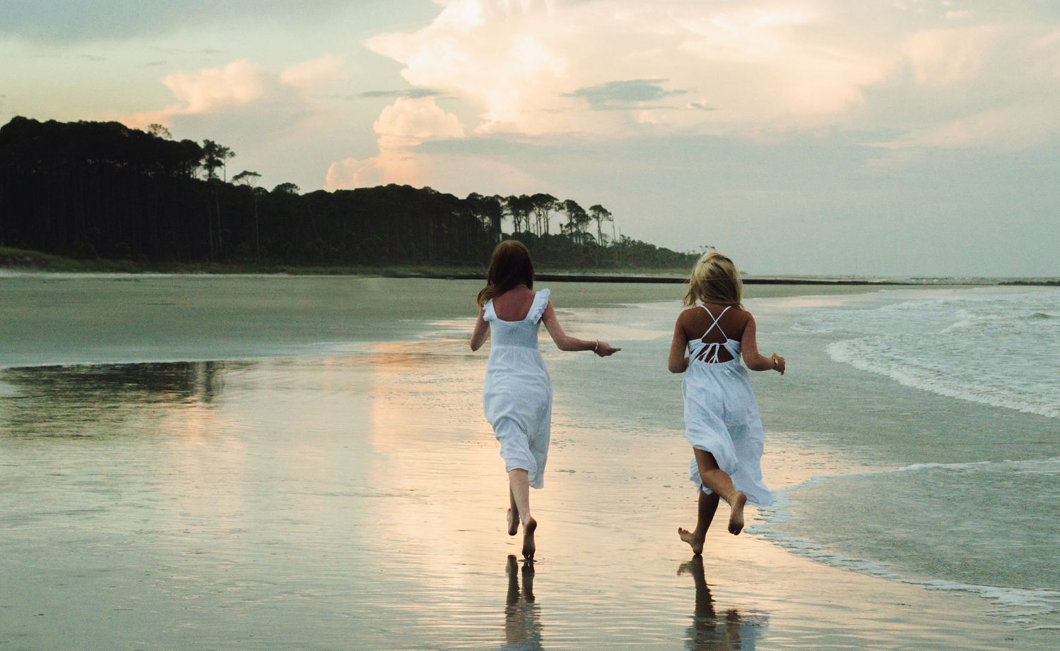 People walking along a tropical beach at sunset with waves lapping at their feet and palm trees in the distance.