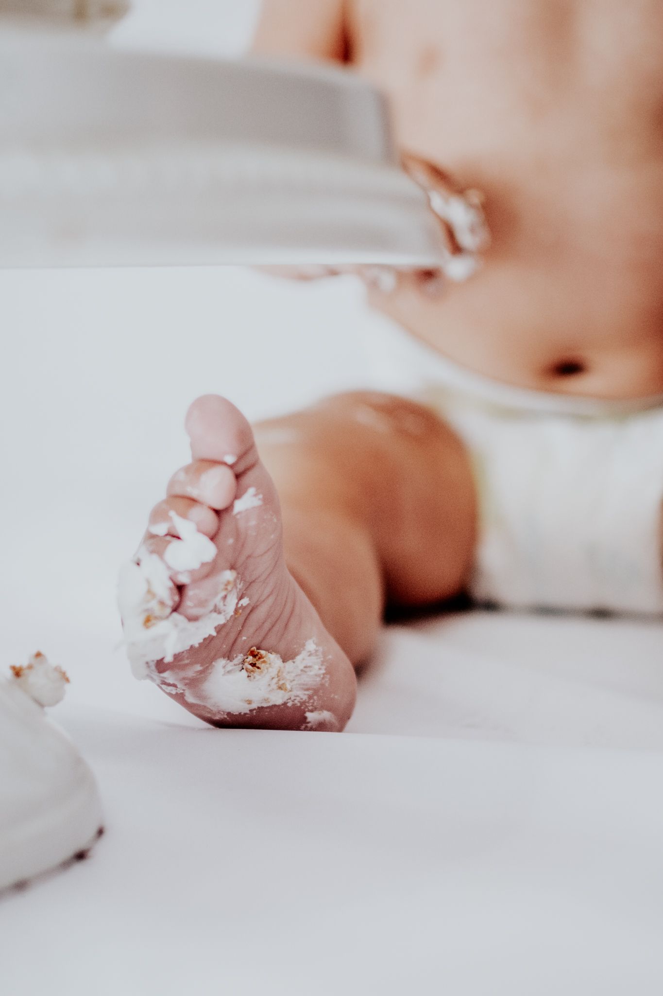 Close up photograph of tiny baby foot covered in white powder against soft white fabric background.