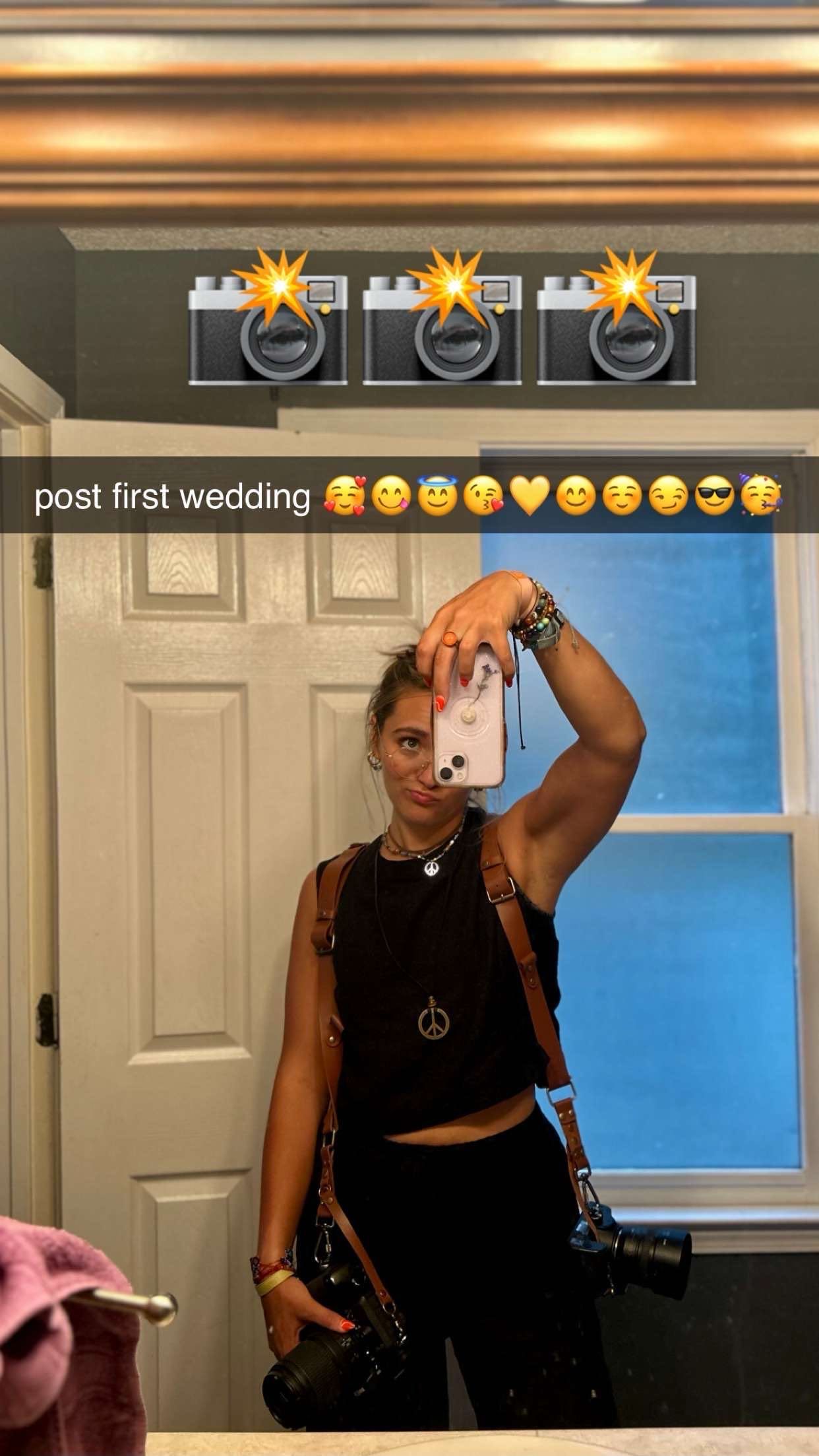Someone takes a bathroom mirror selfie wearing a black crop top outfit while holding up a smartphone camera.