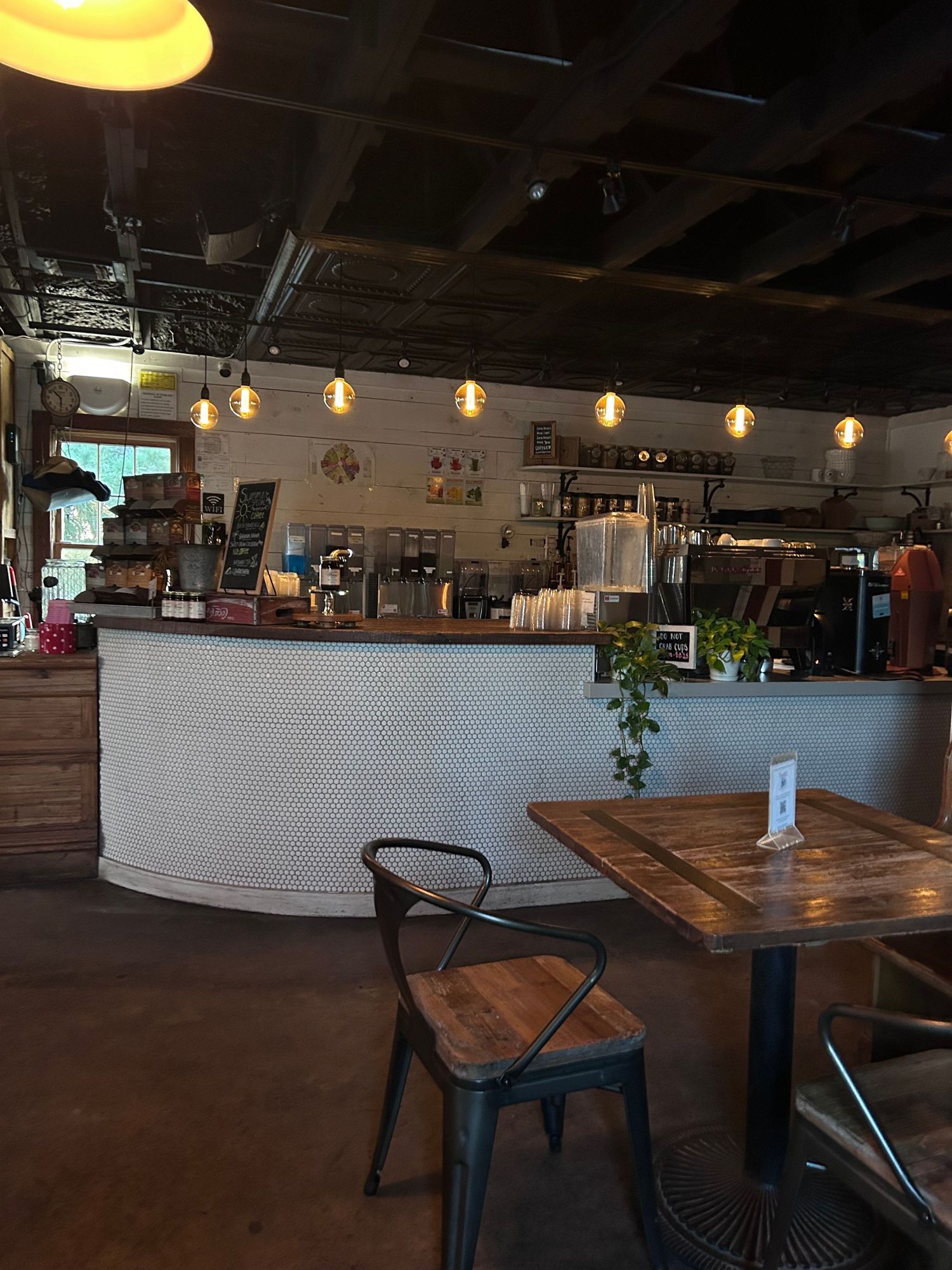 Modern restaurant interior with wooden tables, industrial lighting, and a minimalist bar area at twilight.