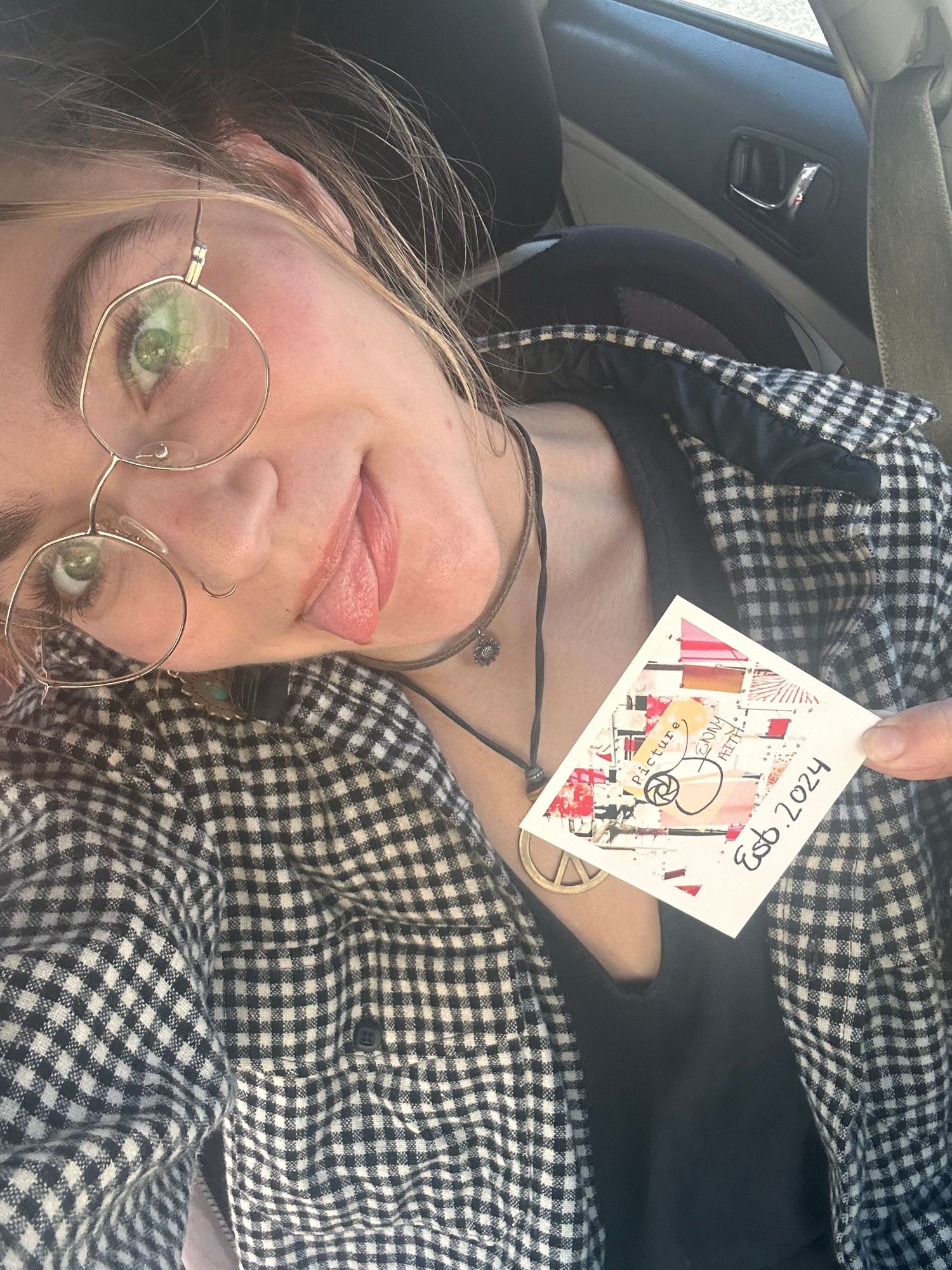 A person in a checkered print top sits in a car holding up a $1 off in'n'out voucher card.