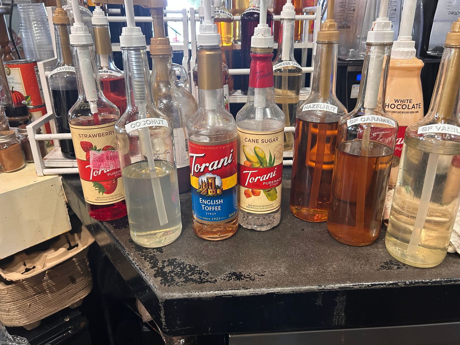 A collection of various liquor bottles and spirits including Torani syrup displayed on a dark counter surface.
