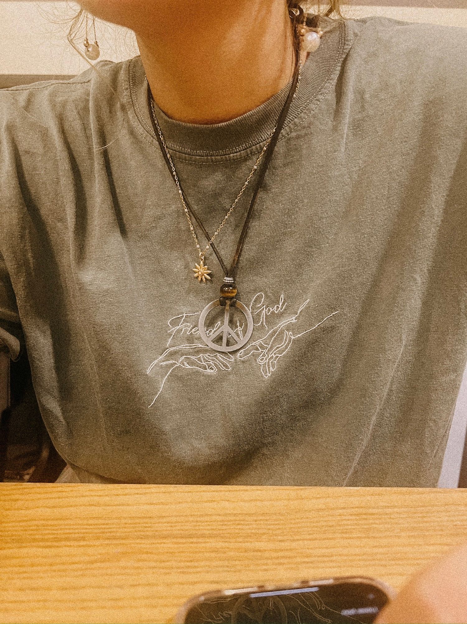 Close-up photo of a gray sweatshirt with peace sign embroidery and layered necklaces featuring sun and peace pendants.