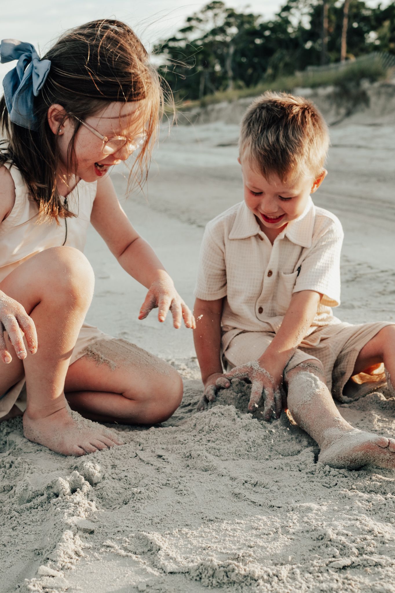 Parent and child playing together in the sand at a beach creating sand castles and formations on a sunny day.
