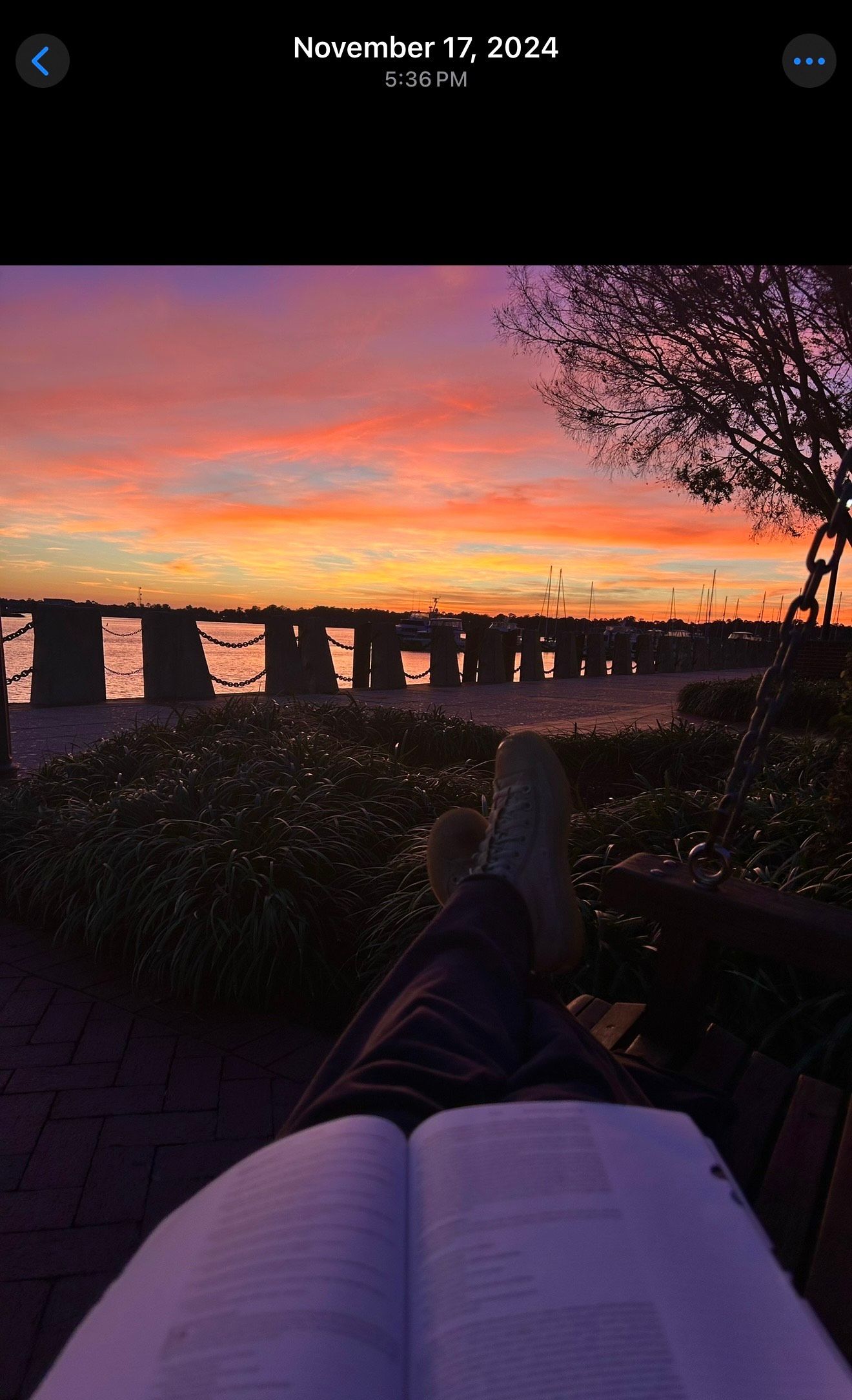 Open book resting on a surface during sunset with vibrant orange and purple sky over water in the background.