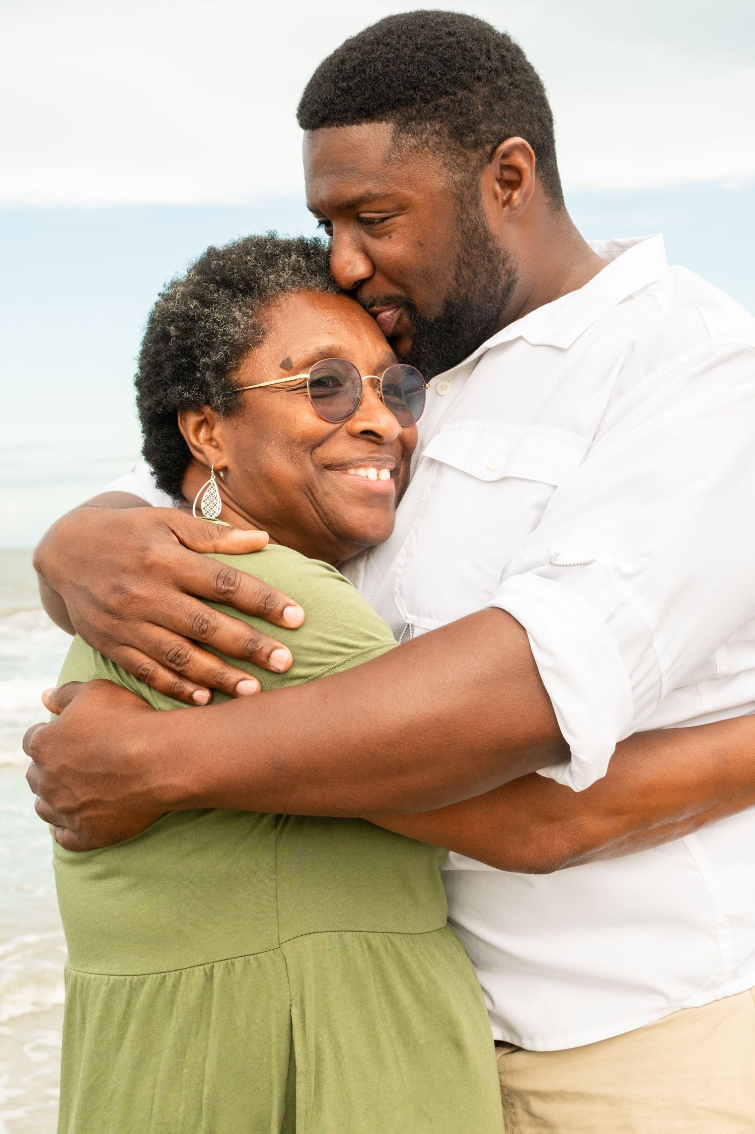 A loving couple embraces on the beach, sharing a tender moment while wearing casual summer attire.