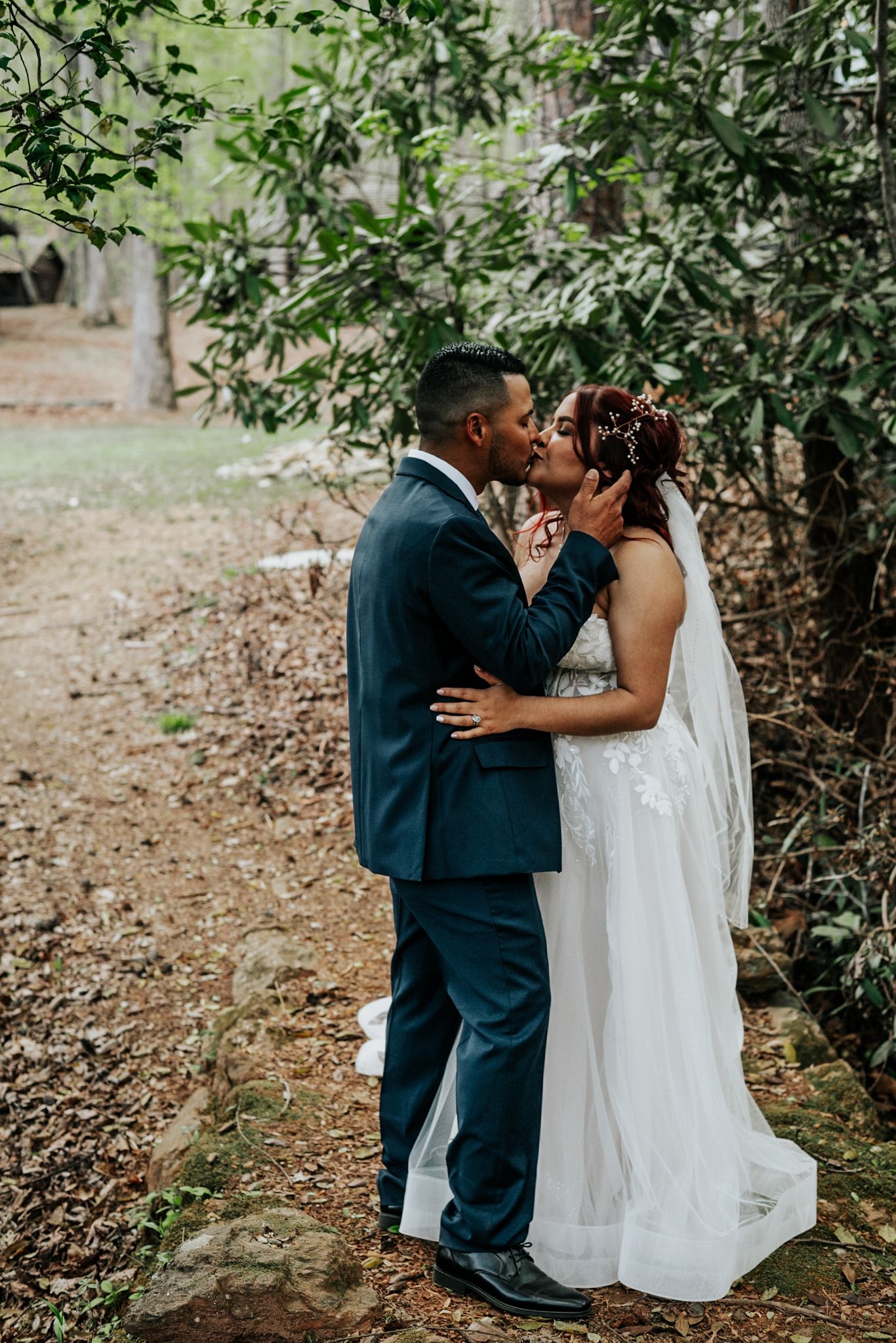 Newlyweds share an intimate kiss on a tree-lined path during their outdoor wedding photoshoot.