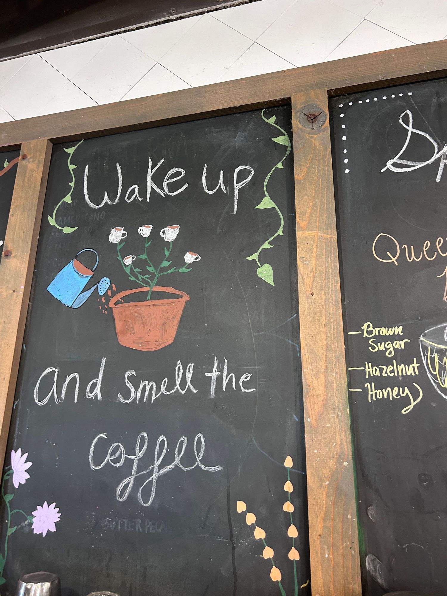 A chalkboard sign with artistic lettering reads 'Wake up and smell the coffee' decorated with floral doodles.