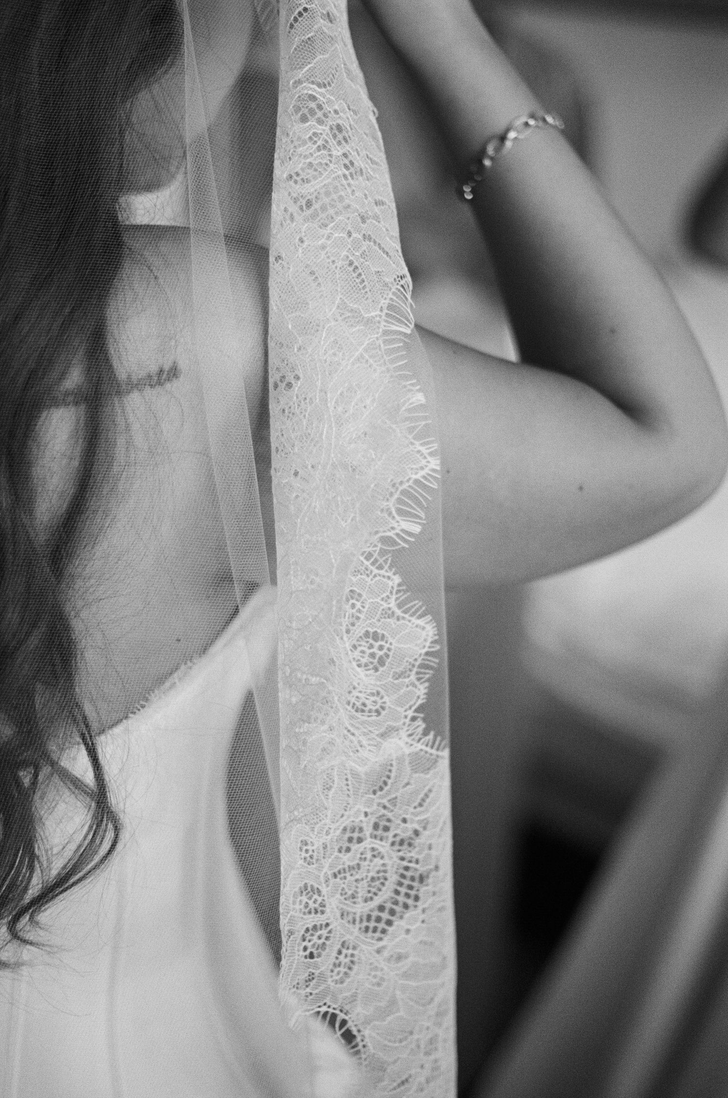 Black and white photo of a bride in a white gown with lace veil detail, showing her back and bracelet.