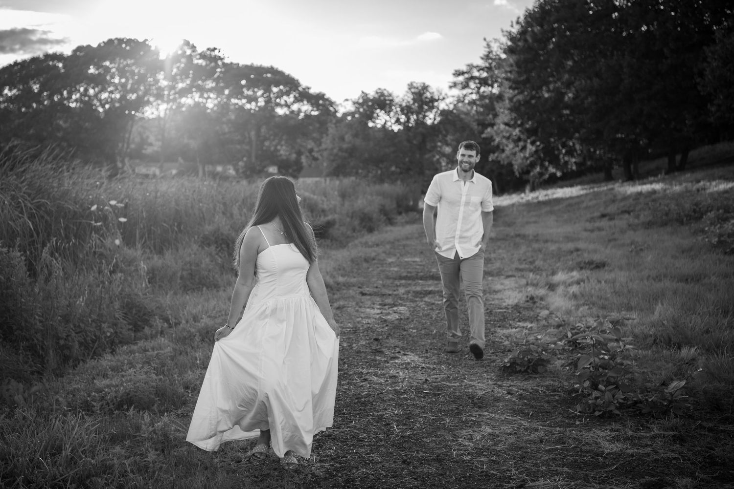 A romantic black and white photo of a couple on a hillside path at sunset.