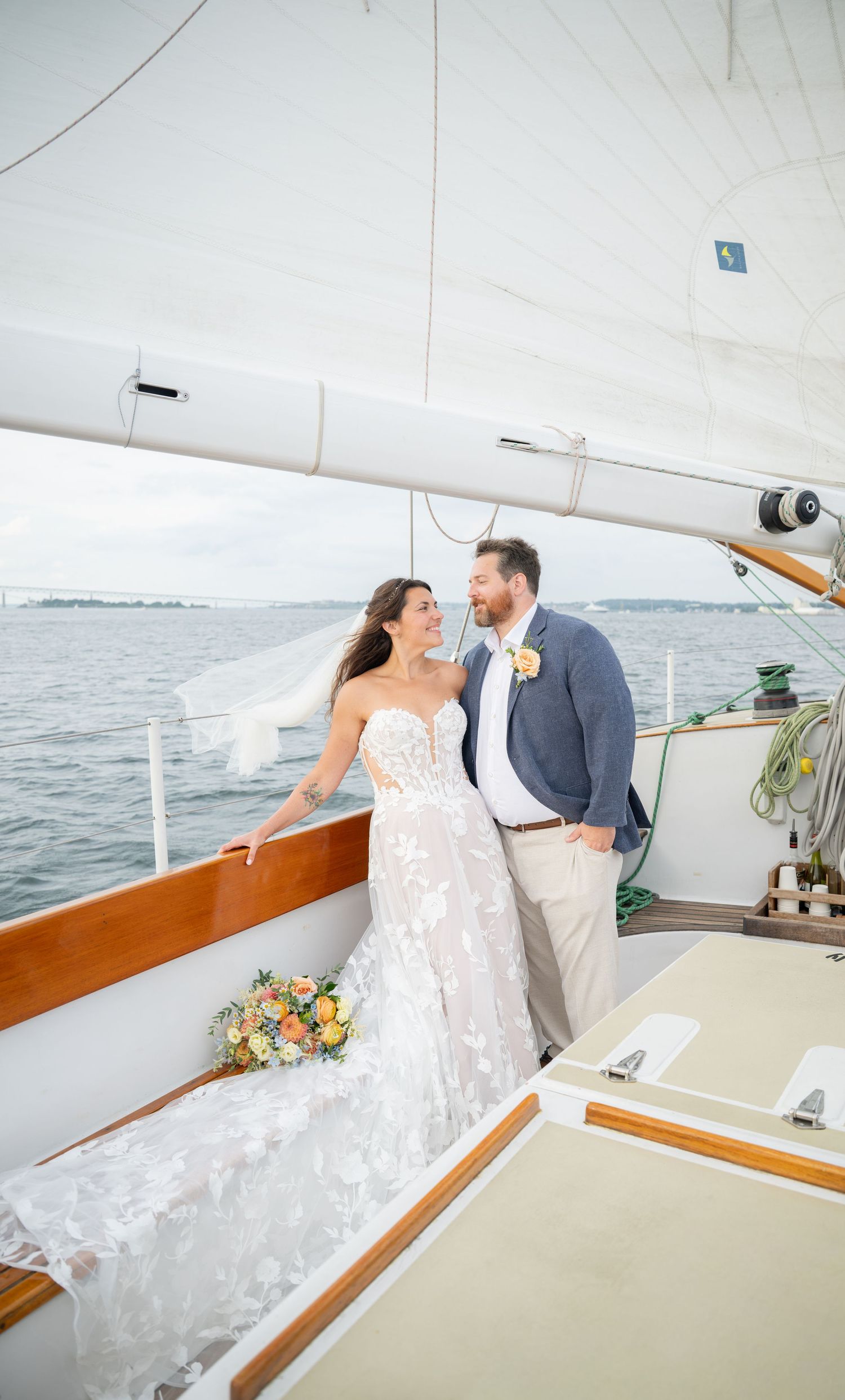 Bride and groom share a romantic moment on a sailboat deck, with white sails and ocean views in the background.