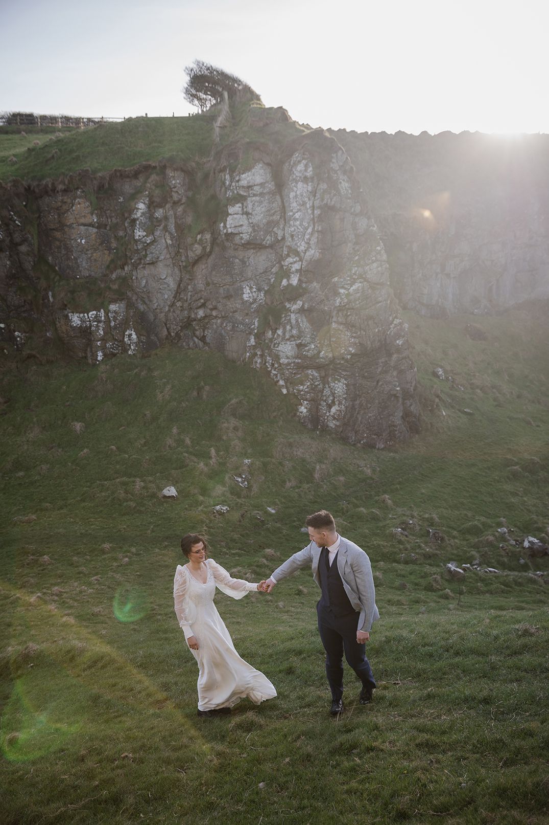 couple holding hands walking through a meadow at the Dunseverick castle by the Causeway coast in Northern Ireland during their elopement