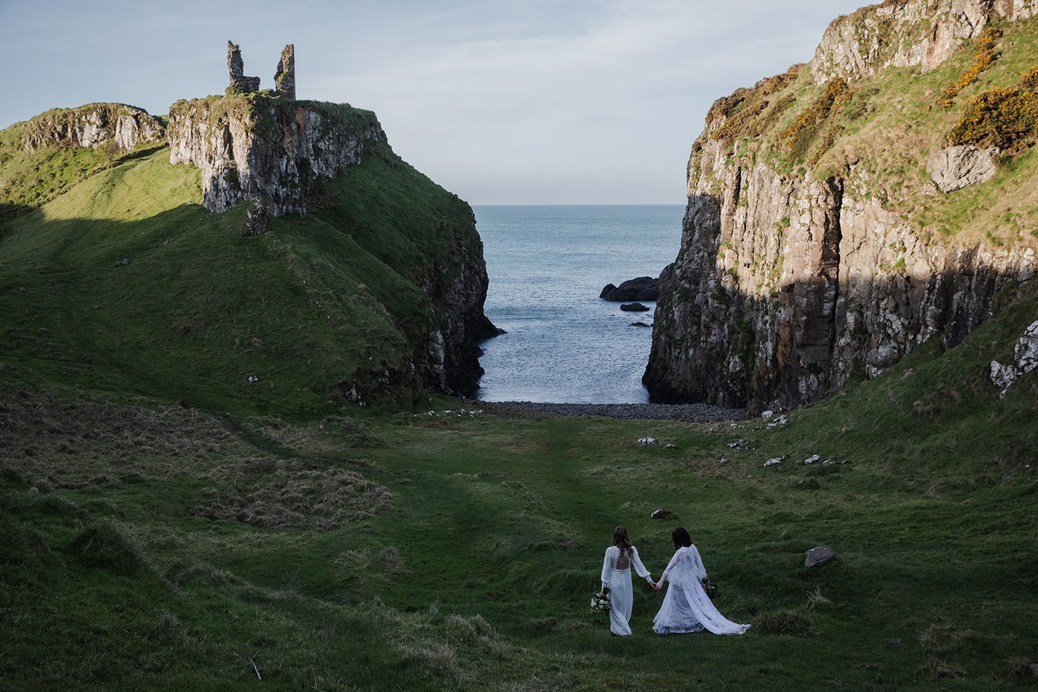 couple holding hands walking through a meadow at the Dunseverick castle by the Causeway coast in Northern Ireland during their elopement