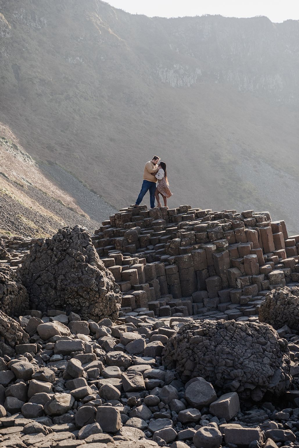 Couple standing on the rocks at the Giant's Causeway, holding each other close during their engagement session in Northern Ireland