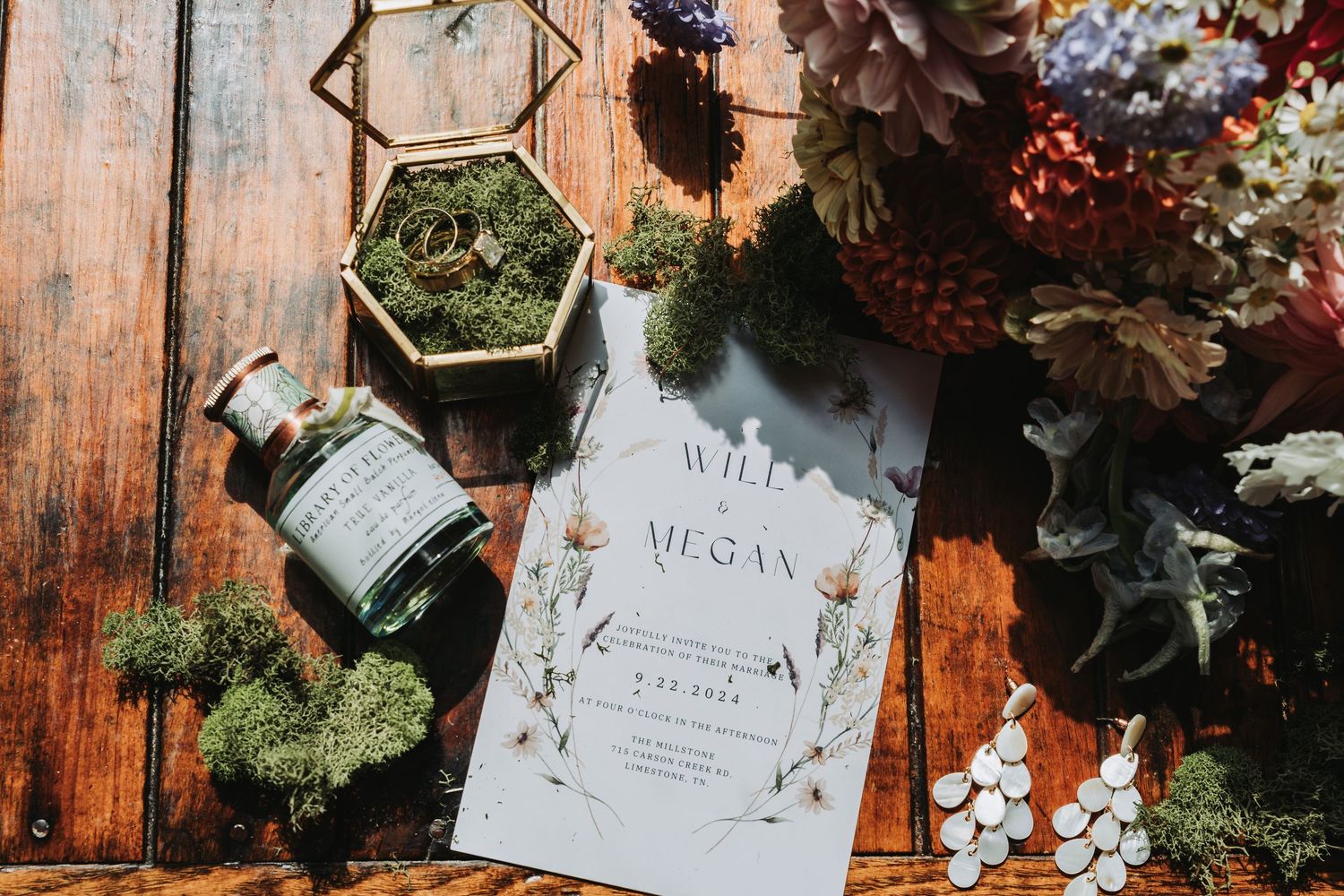 Wedding invitations and floral decorations arranged on rustic wooden table with vintage botanical elements.