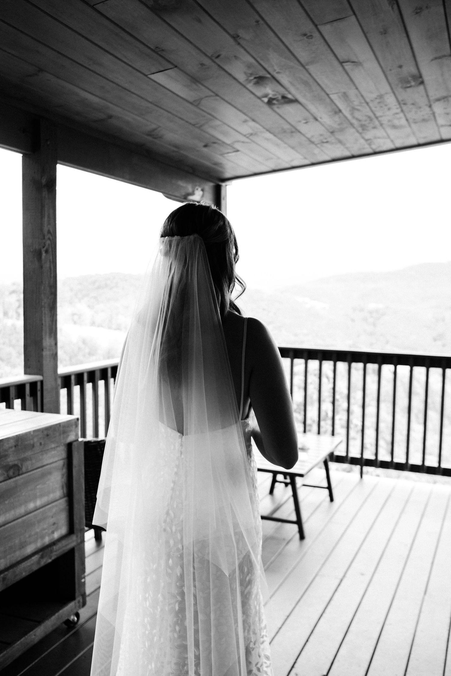 A flowing white wedding veil silhouetted against rustic wooden beams and railings on a covered porch.