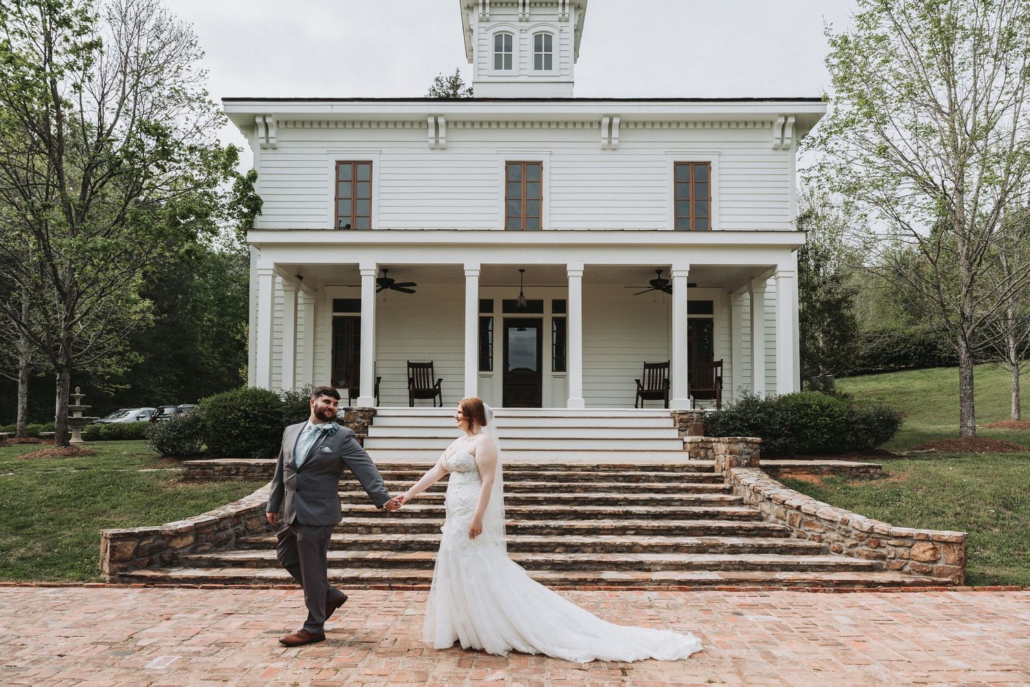 Couple stands at base of elegant white mansion with grand steps and Italianate architecture on their wedding day.