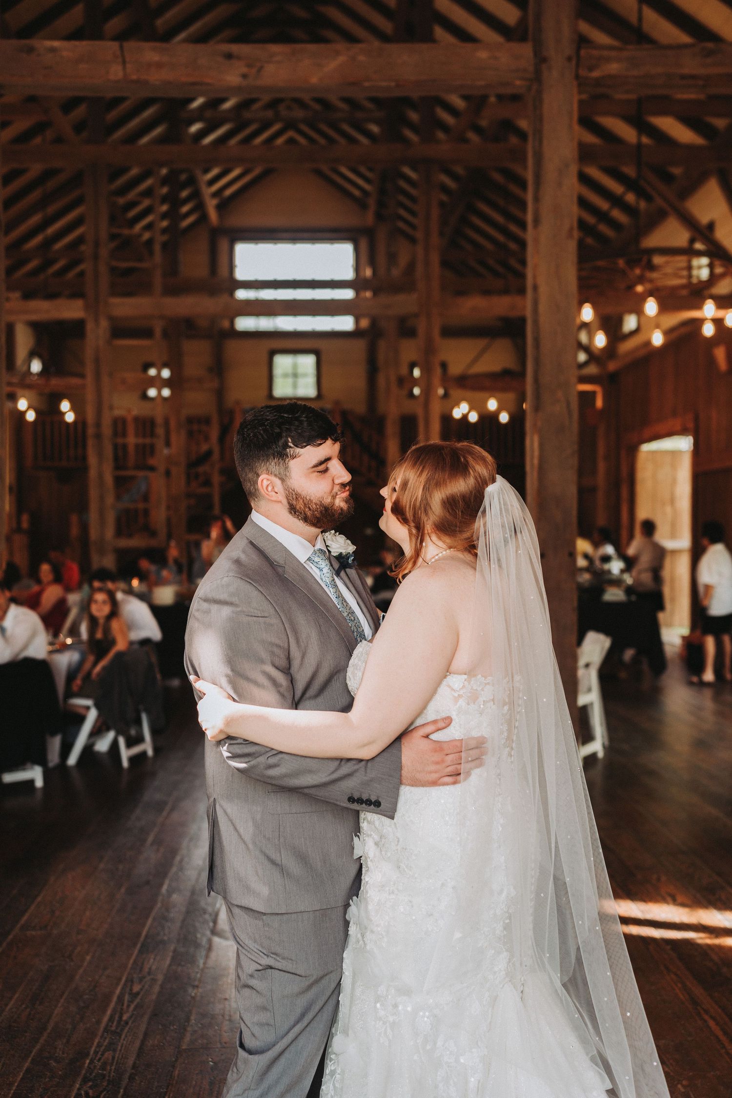 A couple shares their first dance in a rustic barn venue with wooden beams and warm lighting.