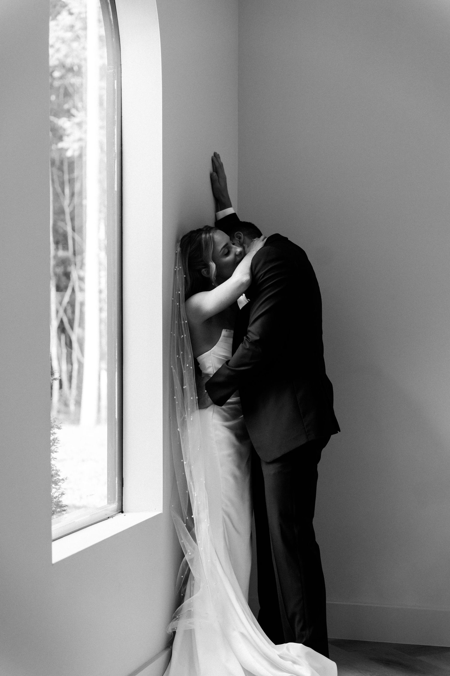 A romantic black and white wedding photo series showing a couple embracing by a window in four sequential shots.