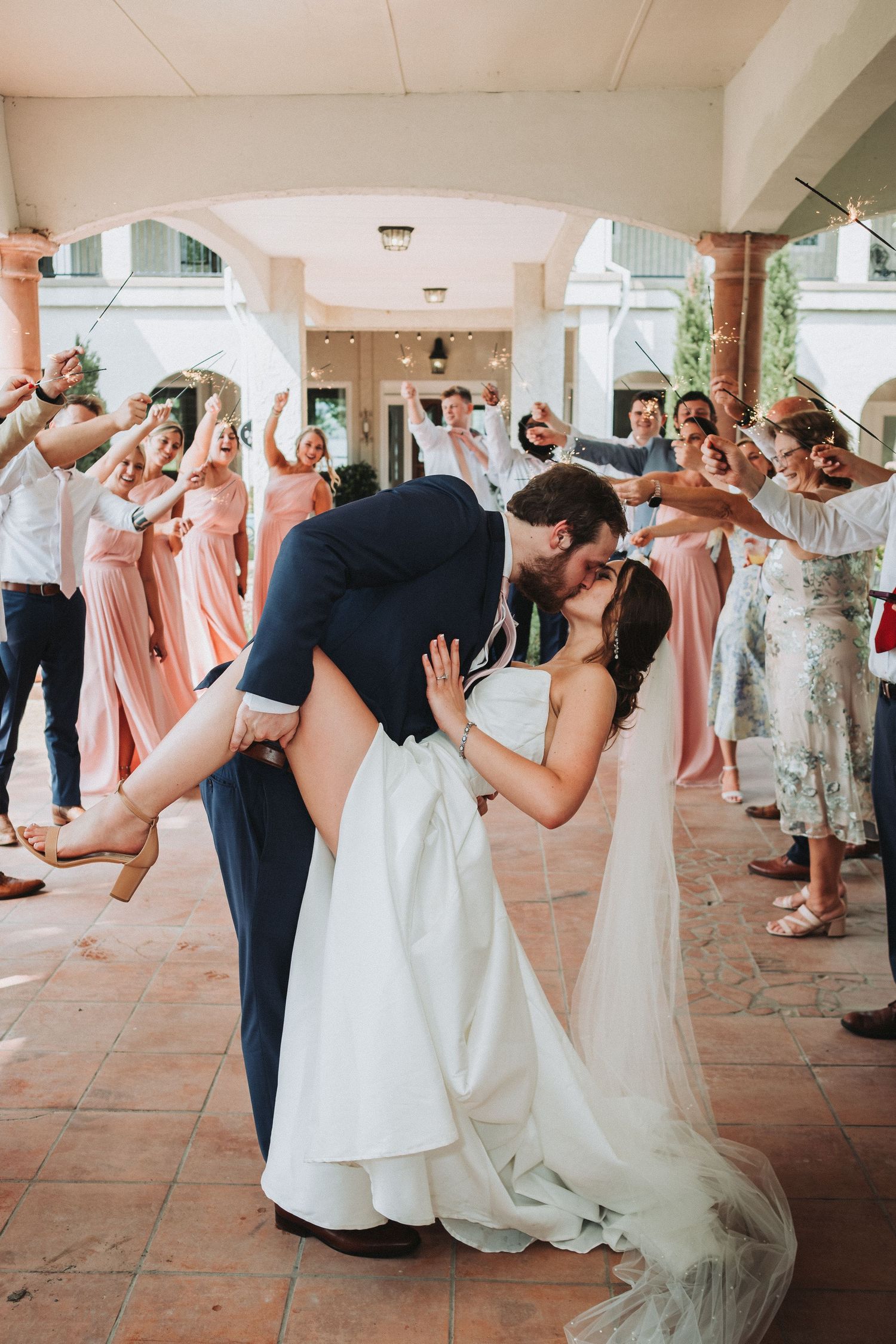 Wedding guests create a celebratory tunnel corridor as couple shares a romantic dip kiss on their special day.