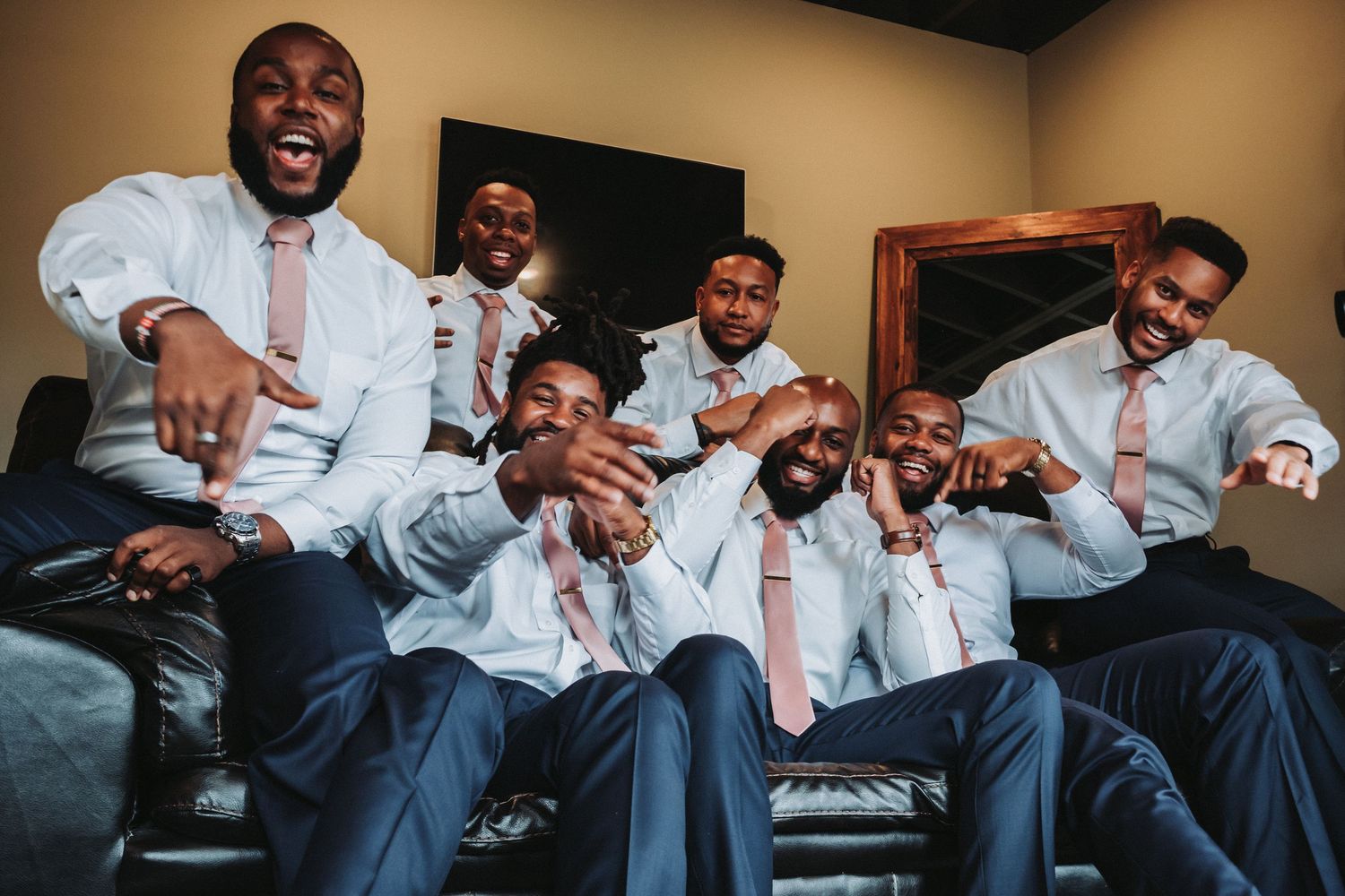 Groomsmen in matching white dress shirts and pink ties pose playfully together for a fun wedding party photo.