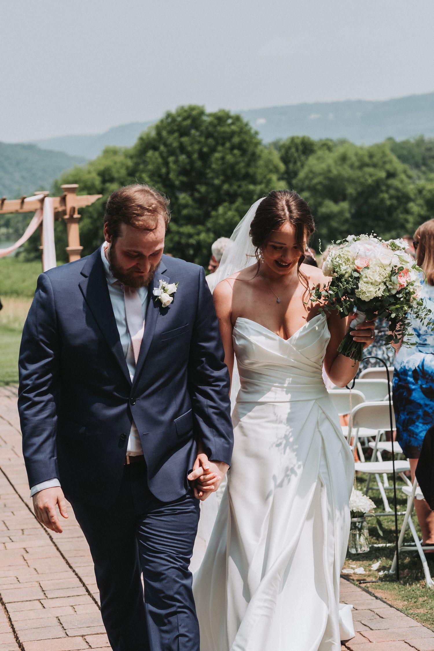 Bride and groom walk together on a brick path with mountain views and wedding ceremony decor visible.