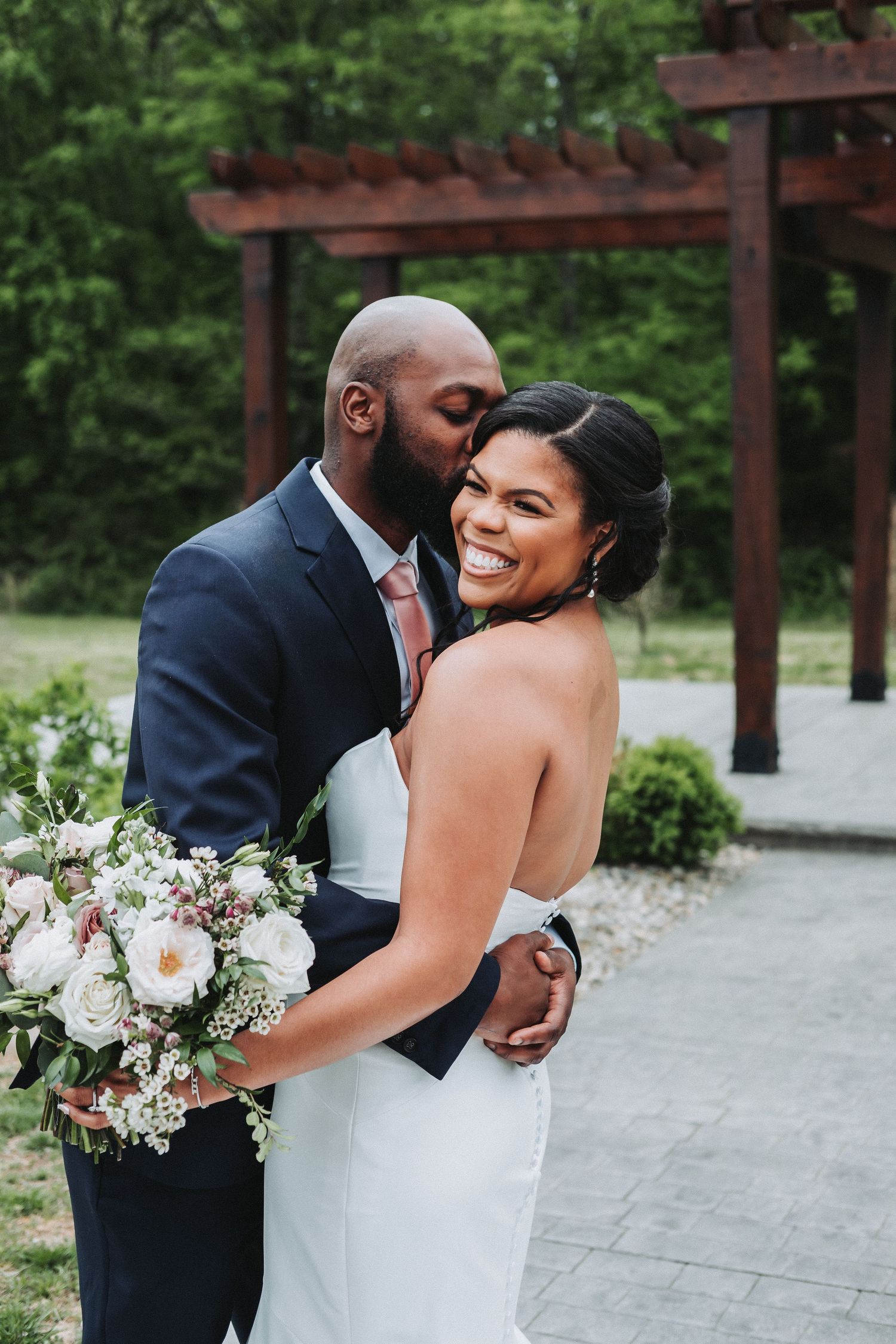 A couple shares a joyful moment outdoors during their wedding, with the bride holding a beautiful floral bouquet.