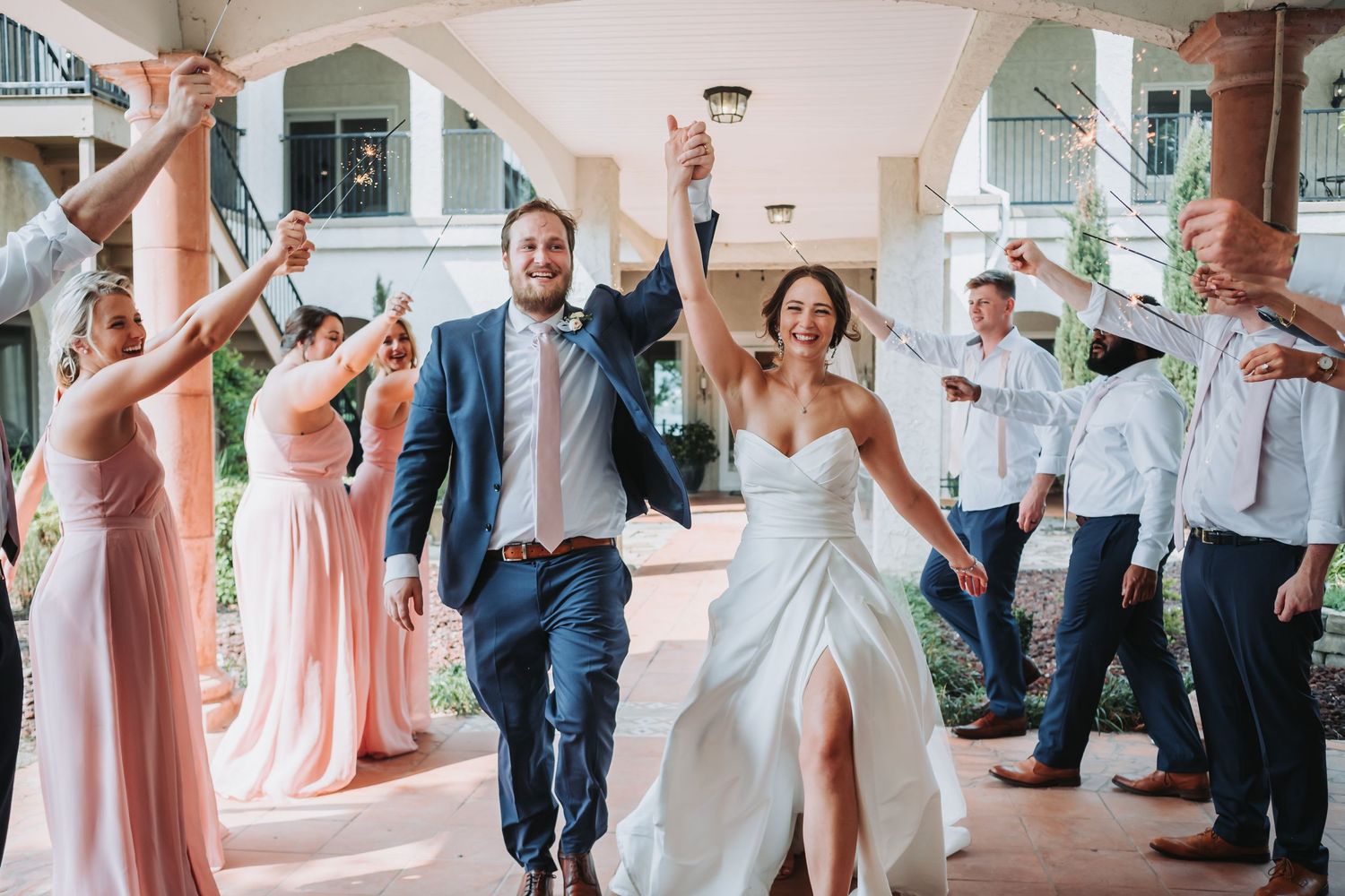 Newlyweds celebrate with guests during their wedding reception as they joyfully walk together down a grand hallway.