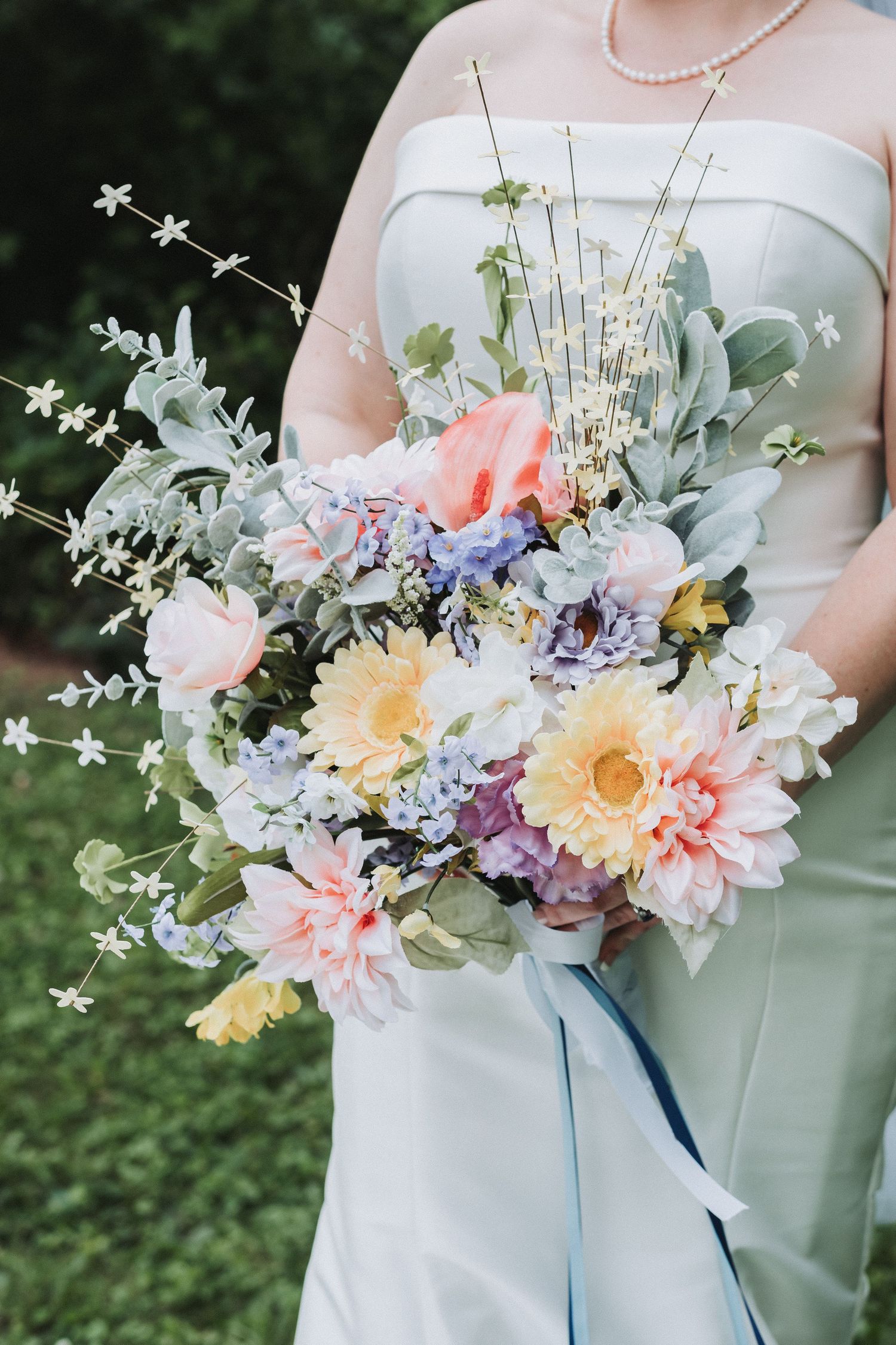 A pastel bridal bouquet featuring pink dahlias, yellow daffodils, blue hydrangeas and silvery eucalyptus tied with blue ribbon.