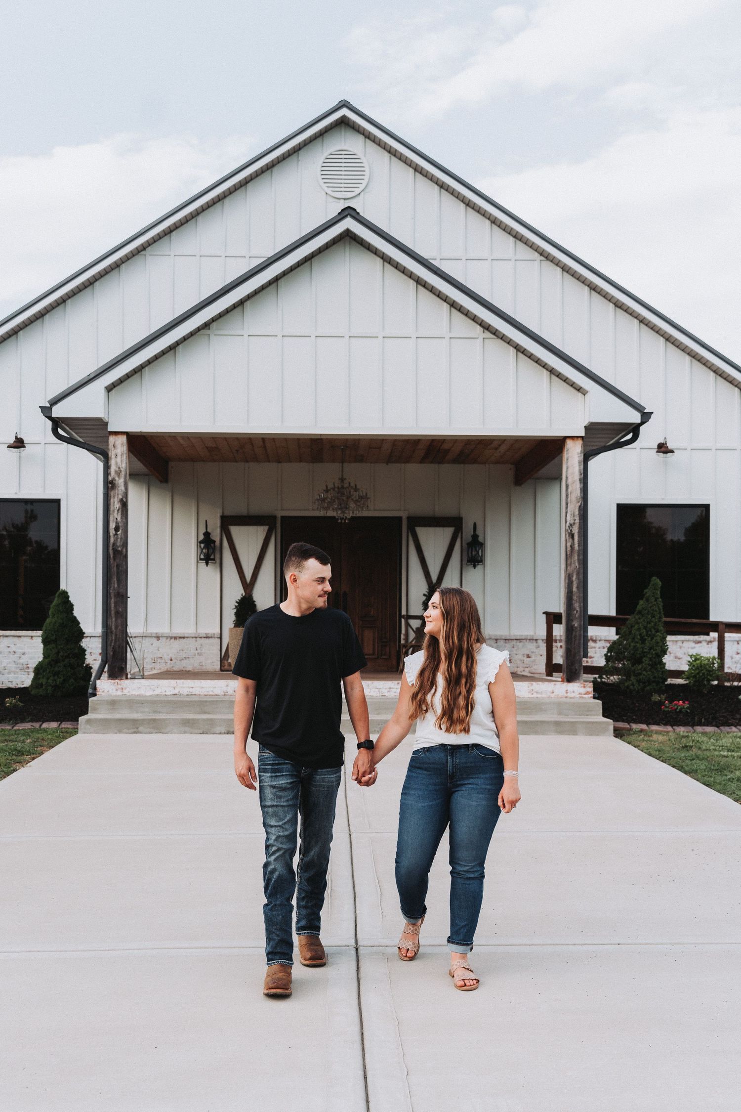 A couple walking away from a modern white barn-style building with black accents and landscaping.